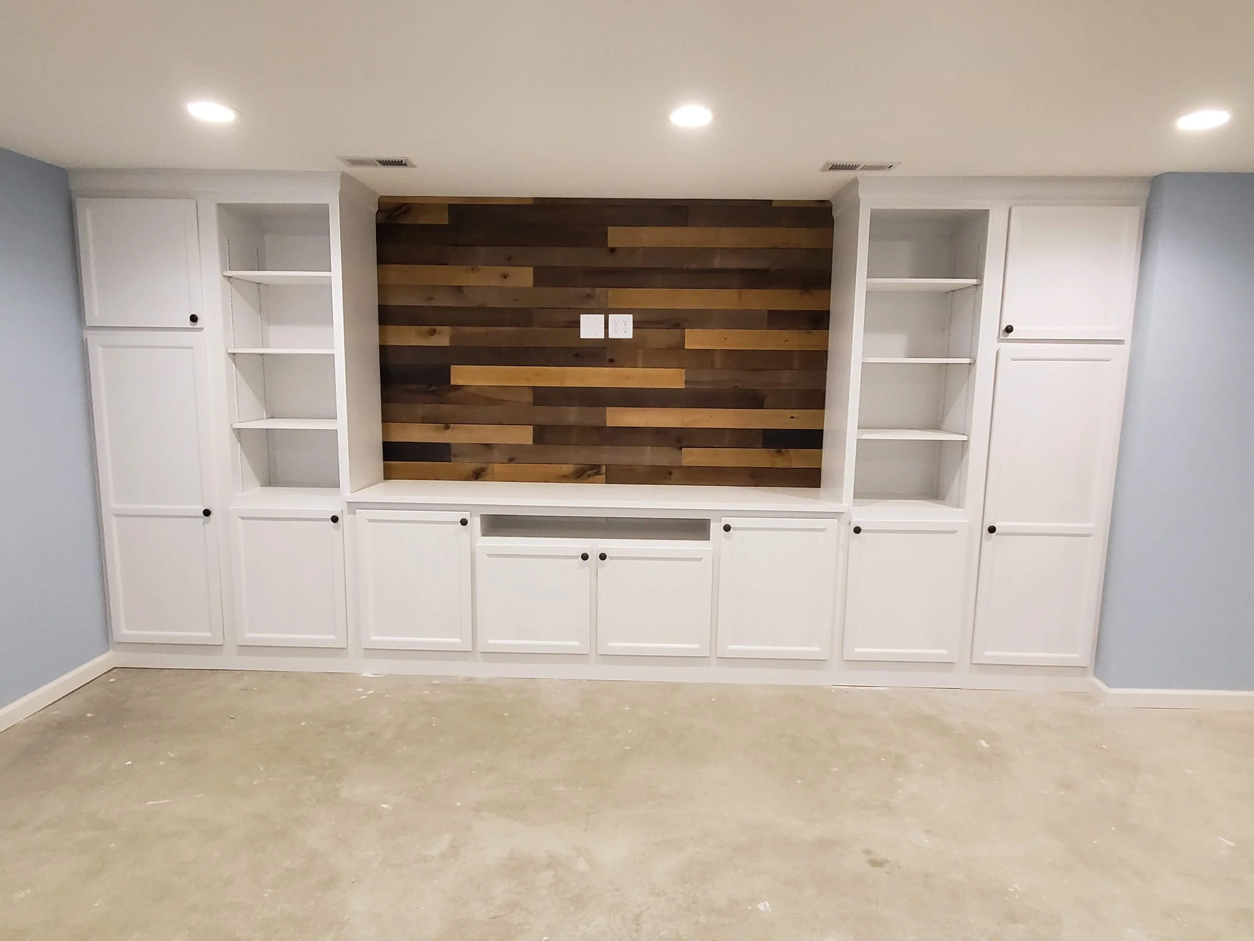 Empty entertainment center with white cabinets and open shelves, wood-paneled wall backdrop.