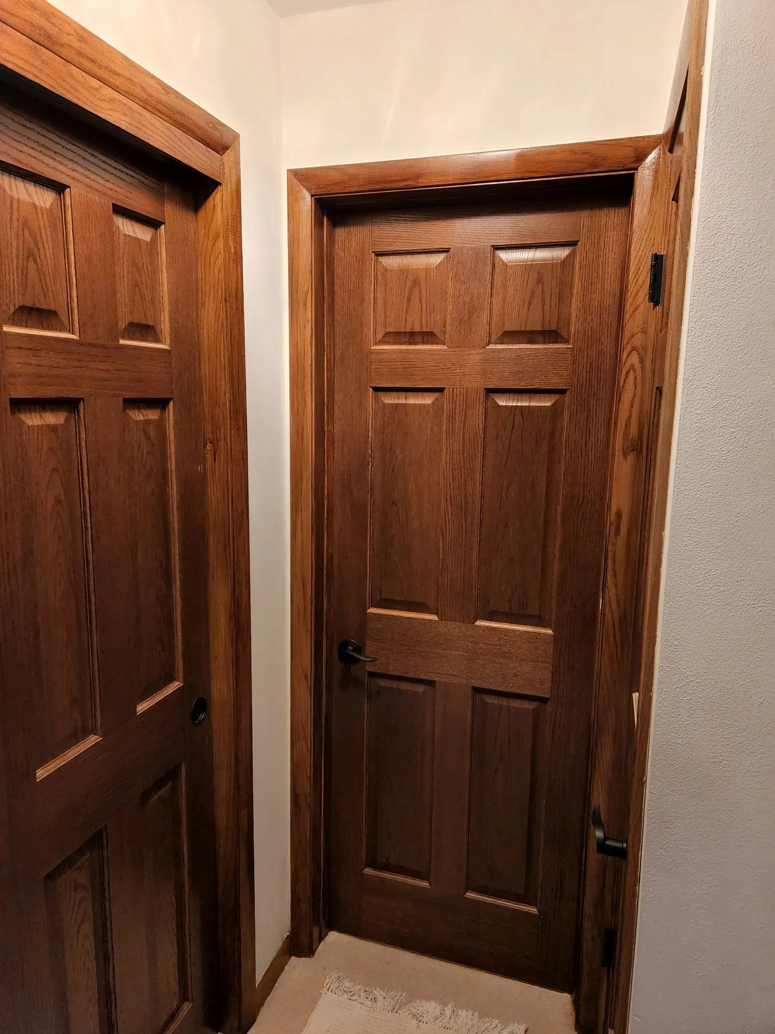 Interior view of a wooden door with a black handle, framed by wood trim, adjacent to another wooden door with a similar design.