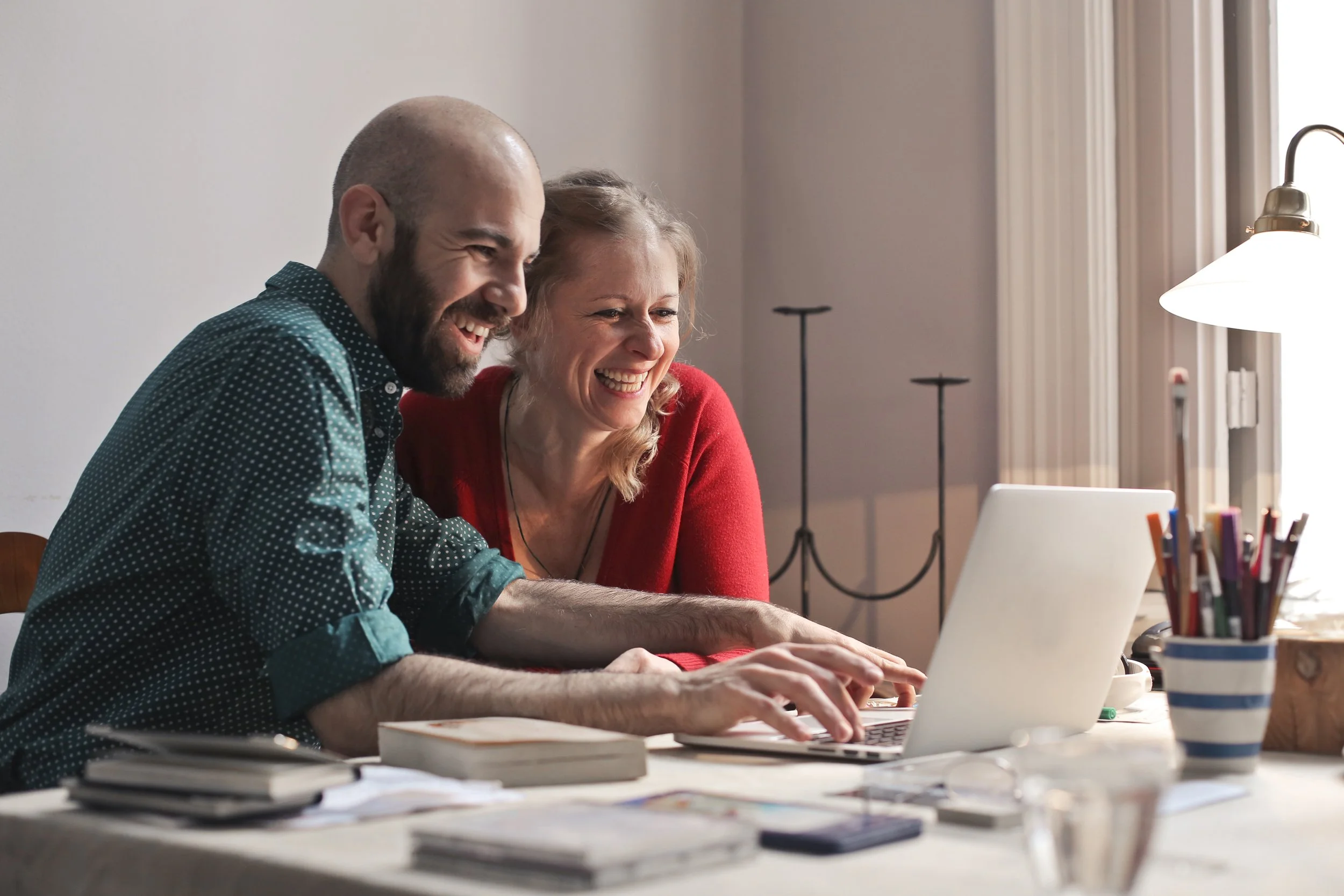 A man and a woman sitting at a table, smiling and looking at a laptop screen.