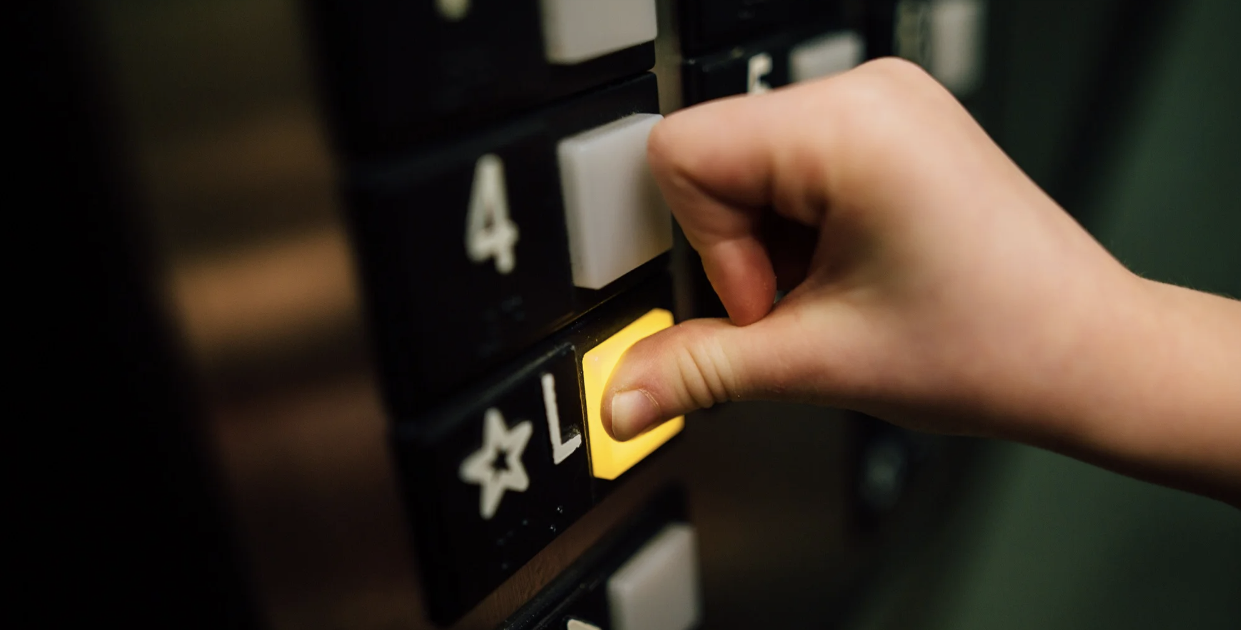 A person pressing a yellow button labeled 'L' on an elevator control panel.