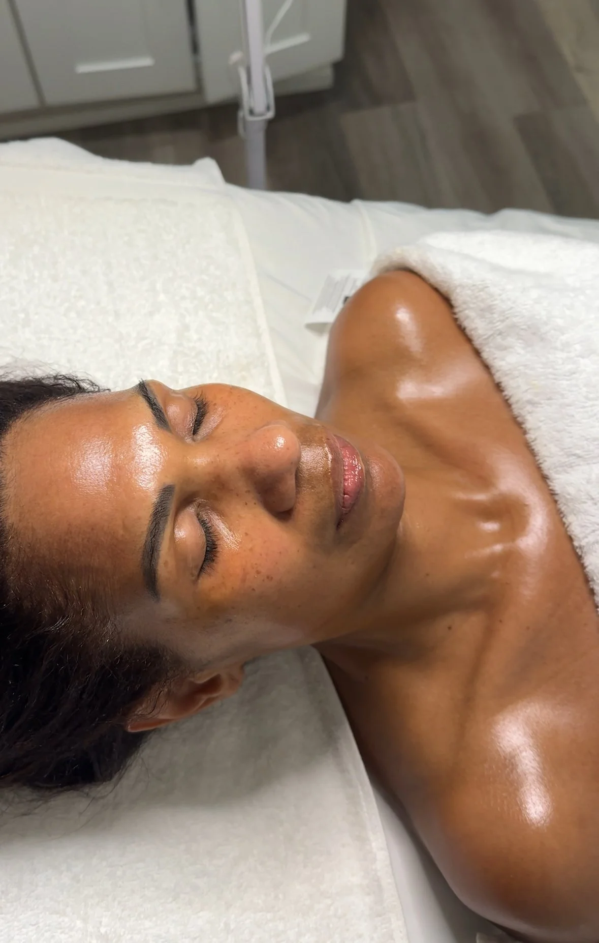 A woman lying on a medical bed, with her eyes closed, in a spa or clinic setting, possibly after a treatment.