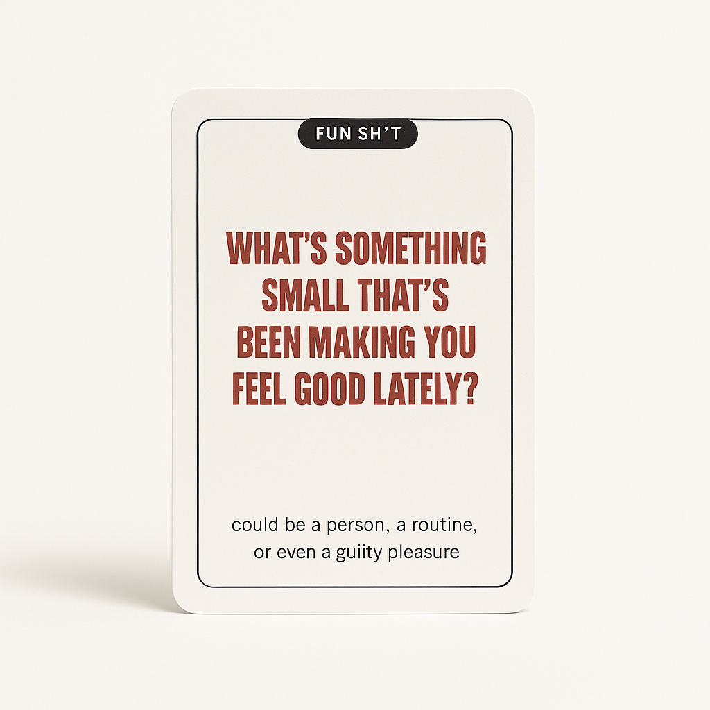 A white card with black, red, and gray text that reads, 'FUN SH'T. WHAT'S SOMETHING SMALL THAT'S BEEN MAKING YOU FEEL GOOD LATELY? Could be a person, a routine, or even a guilty pleasure.' The card is standing against a plain white background.