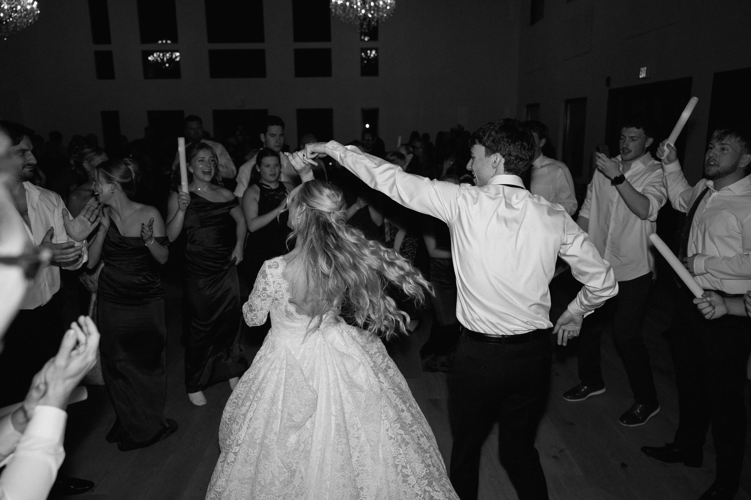 Couple dancing at wedding reception, surrounded by guests in black and white photo.