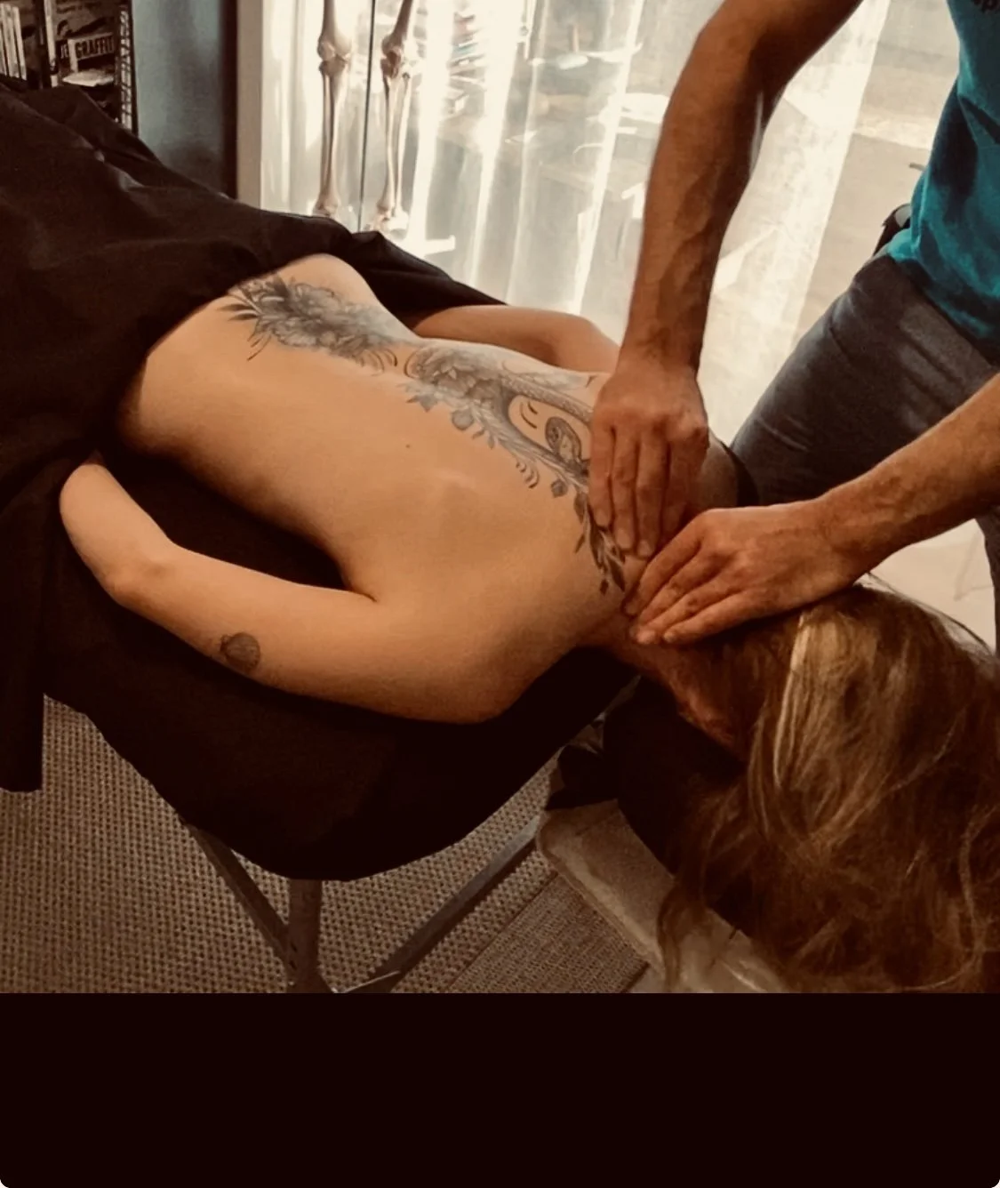 Une femme est allongée sur une table de massage, recevant un massage des épaules, semblant détendue avec les yeux fermés. Un thérapeute asiatique lui masse les épaules dans une salle de massage en bois avec un tapis en fibre naturelle.