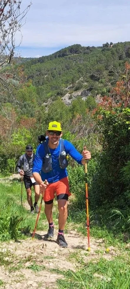 Deux personnes qui font de la randonnée en montagne, avec un en arrière-plan un paysage de forêt et de collines verdoyantes. Grand Raid du Ventoux by UTMB