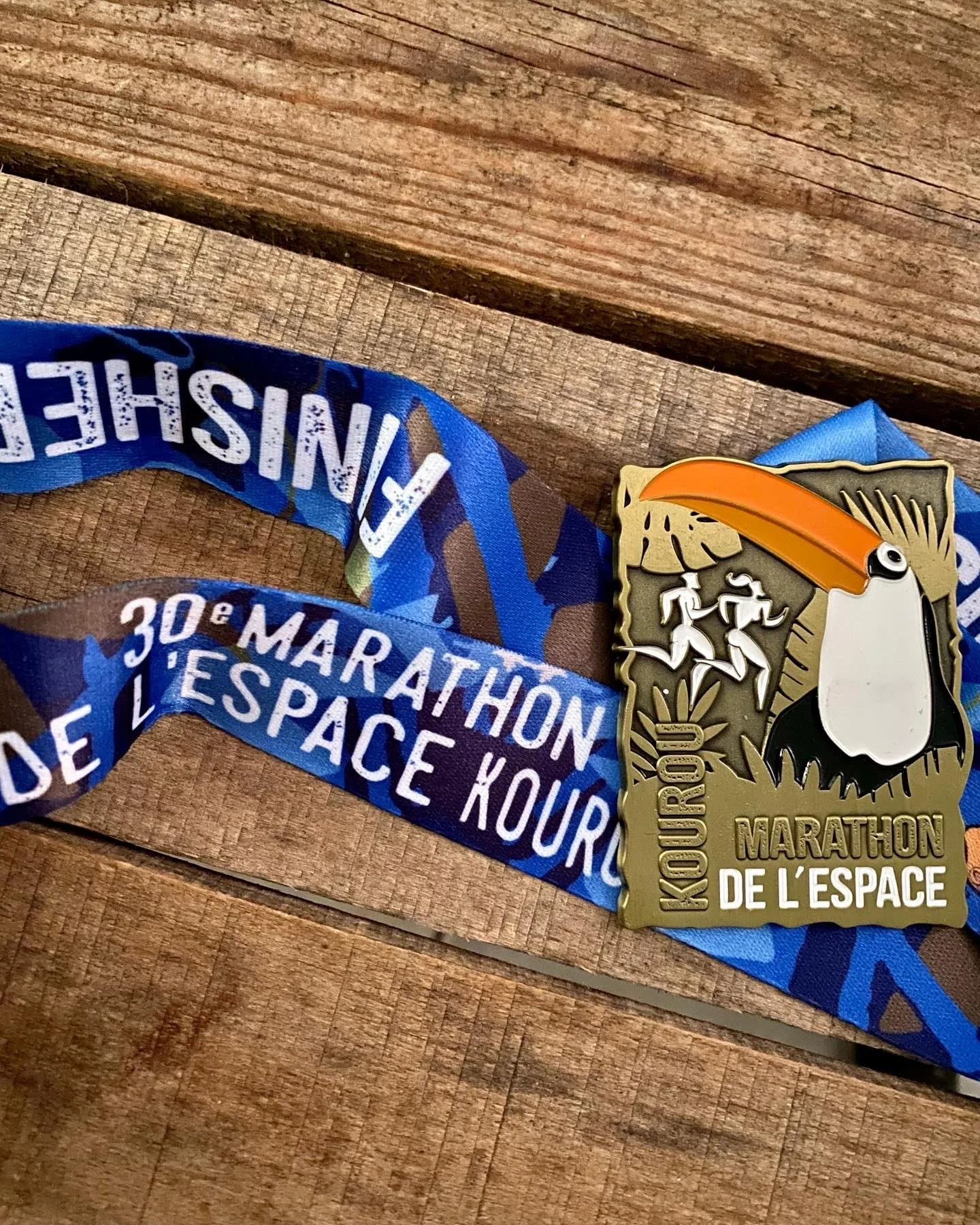 Une médaille de course marathon avec un toucan stylisé, une banane, deux coureurs et le texte 'Marathon de l'espace' et 'Kourou'.