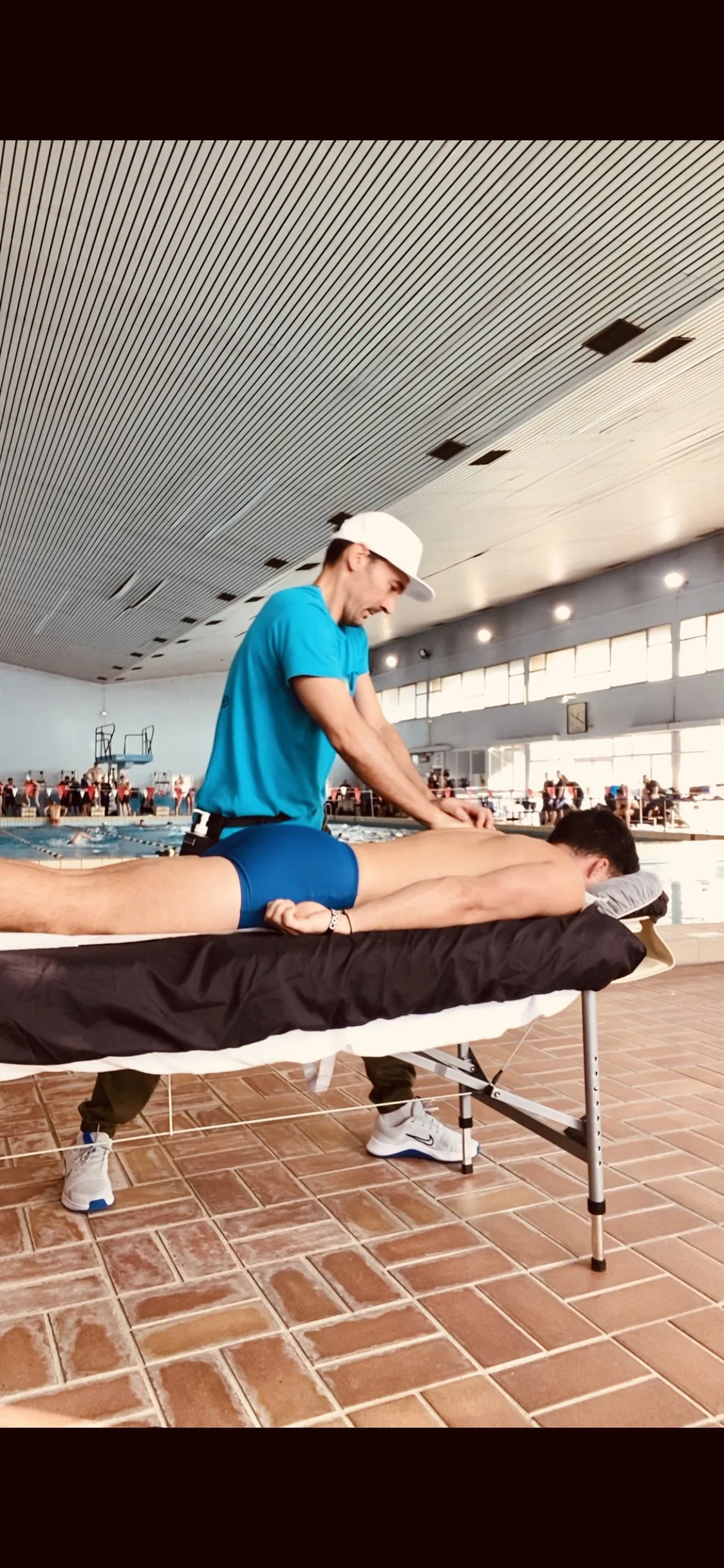 Un homme pratique une séance de massage ou de thérapie sur une femme allongée sur une table de massage dans un environnement naturel avec des plantes tropicales en arrière-plan.
