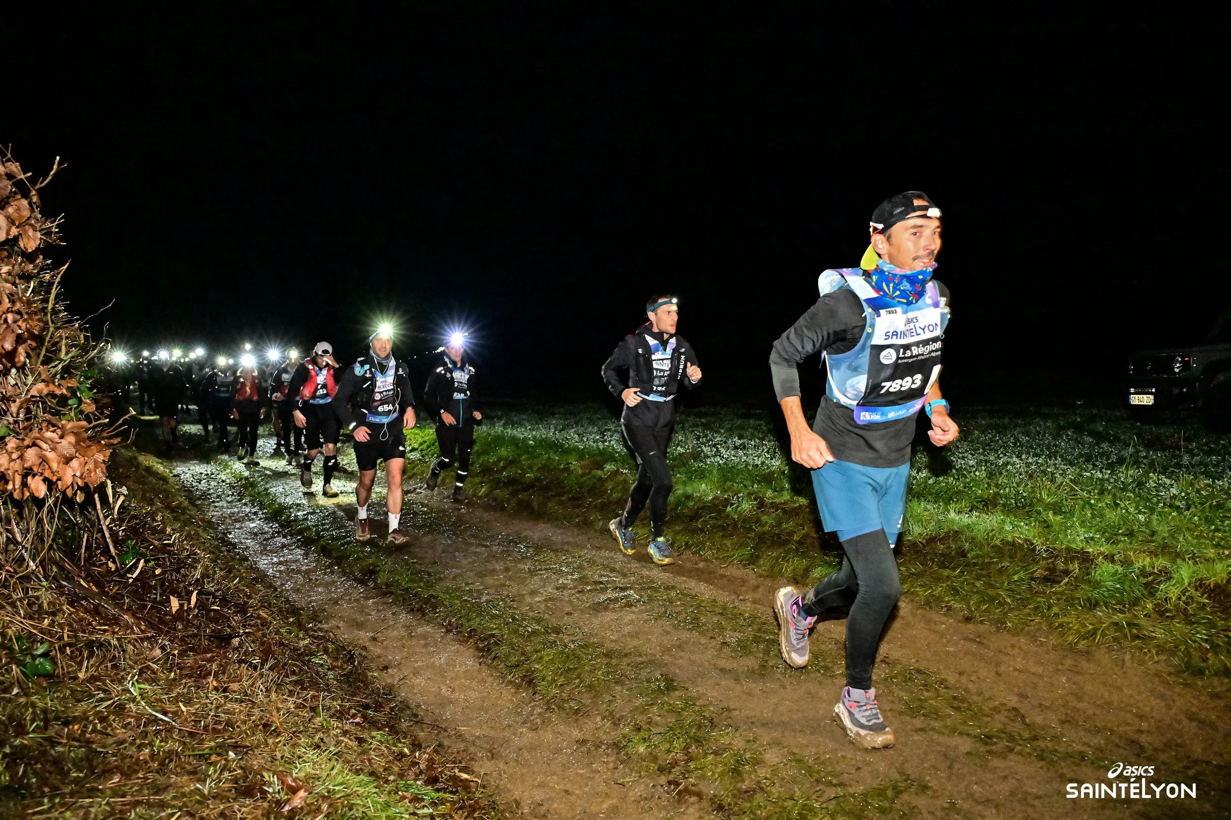 Groupe de coureurs participant à une course de nuit dans un environnement sombre, certains portant des lampes frontales et des équipements sportifs. Course SaintéLyon 2025