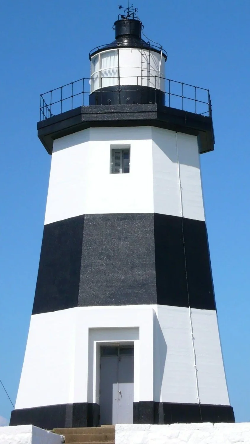 A black and white striped lighthouse against a clear blue sky.