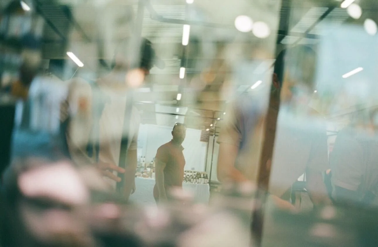 People walking in a modern indoor space, seen through a reflective glass surface.