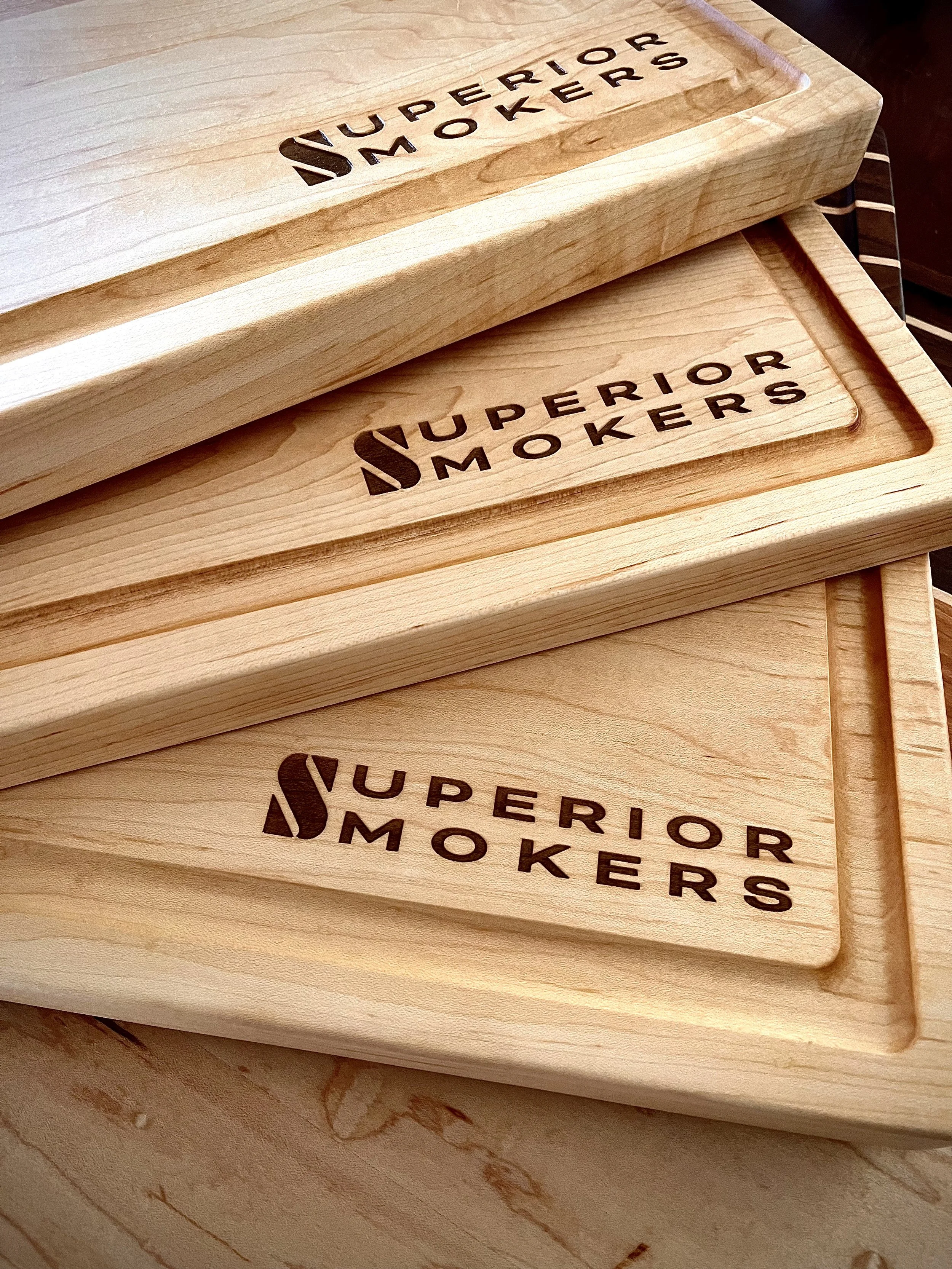 Three wooden cutting boards with the brand name 'Superior Smokers' engraved on them, stacked on top of each other.