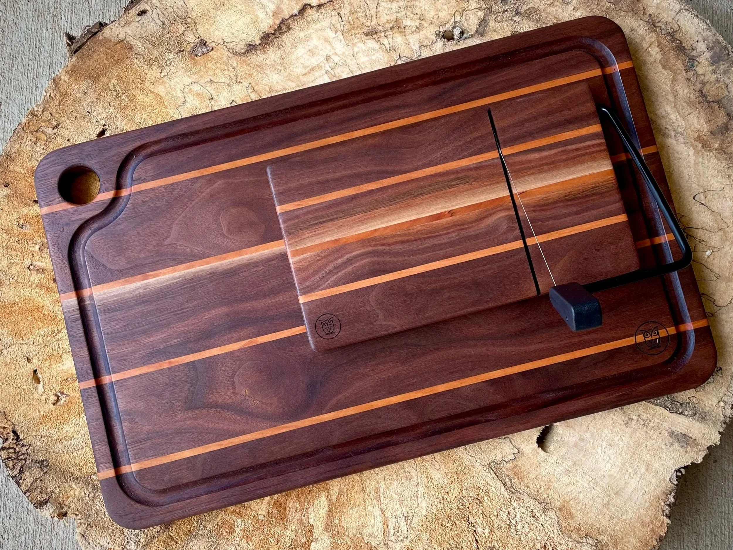 Wooden cutting board with a sliding cover, a handle, and a black slicer knife, placed on a wooden surface.