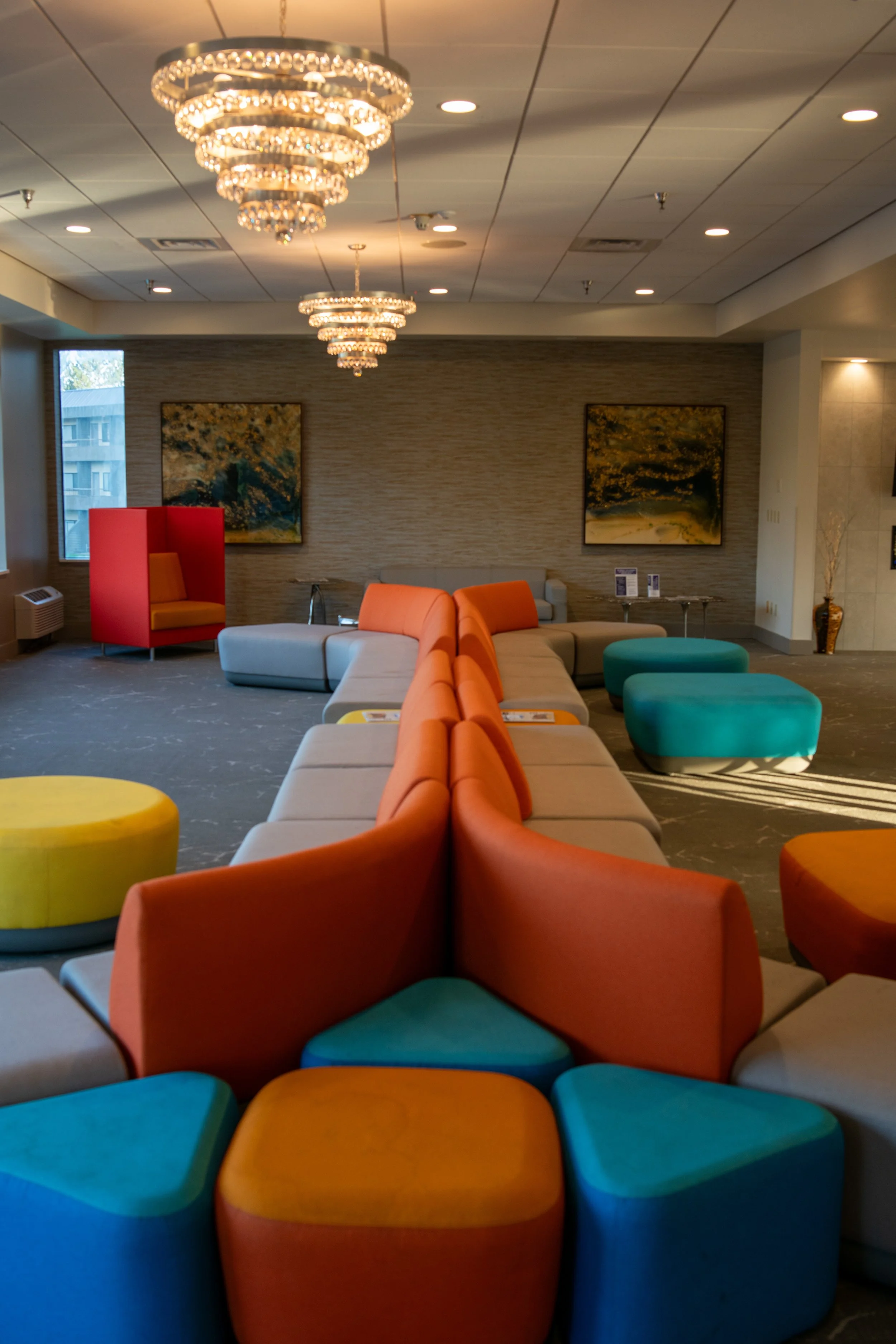 Colorful modern lobby with a variety of shaped, brightly colored seating, paintings on the wall, and a chandelier overhead.