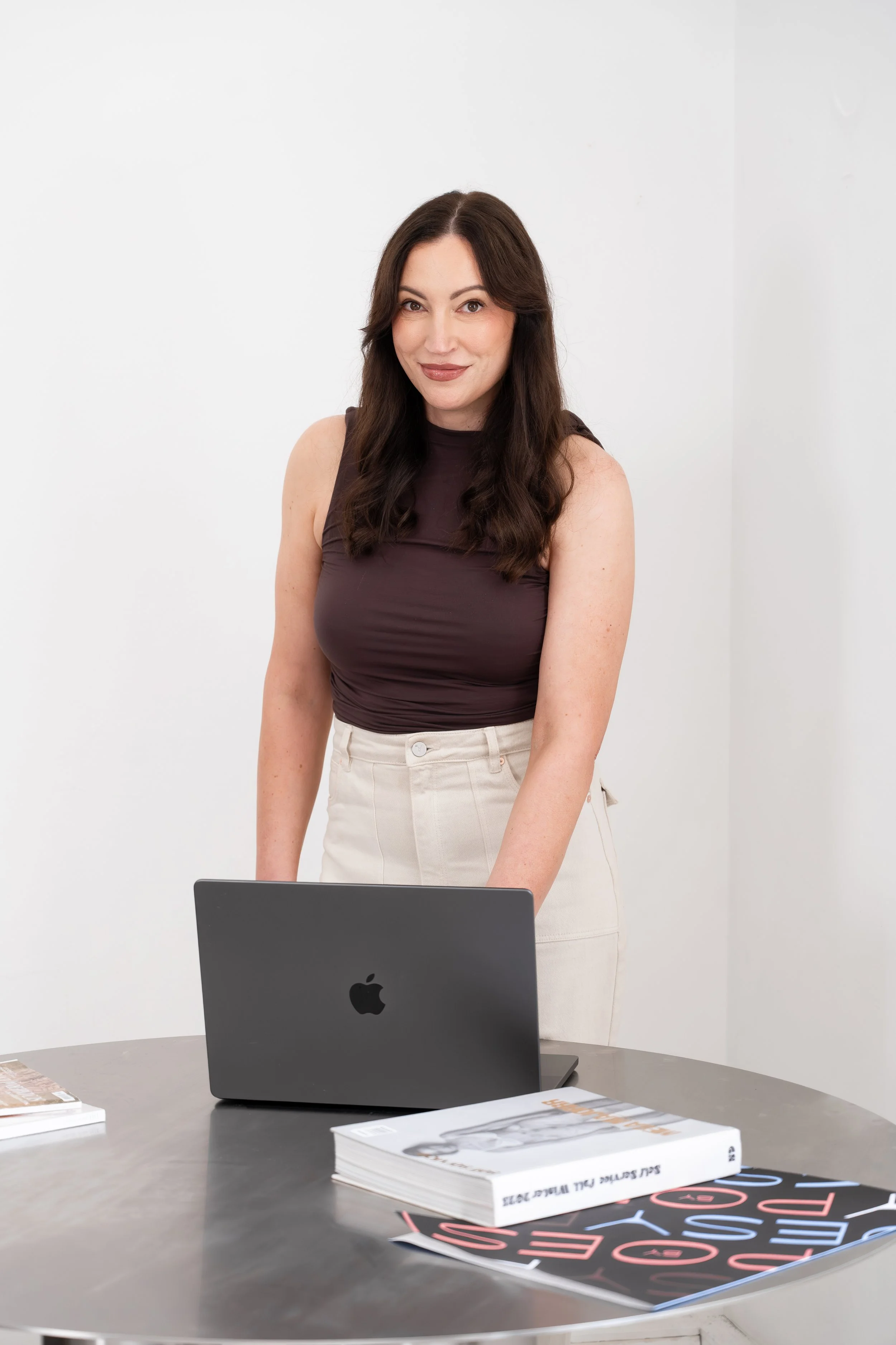 Melanie, graphic and web designer, seated in a studio reading a magazine in a bright, minimalist space.