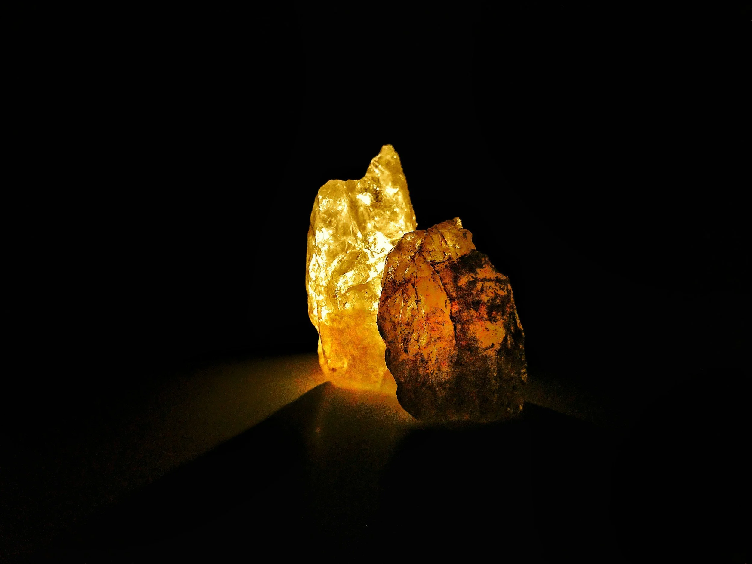 Two glowing salt crystals, one slightly yellow and the other orange, illuminated in a dark environment.