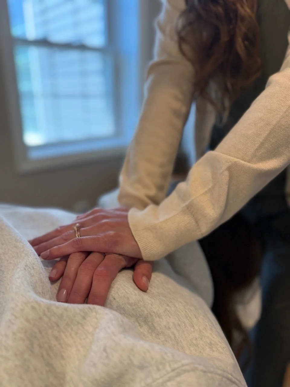 Person performing a massage on another person's back in a well-lit room near a window.