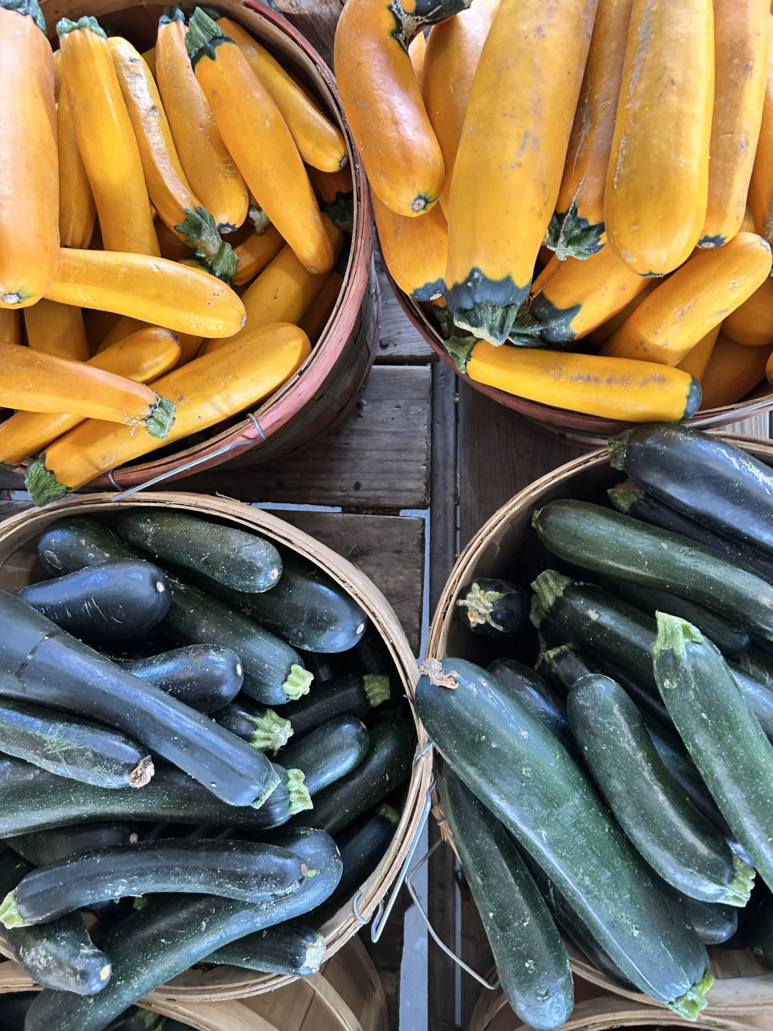 Baskets of yellow squash and zucchinis on a wooden table.