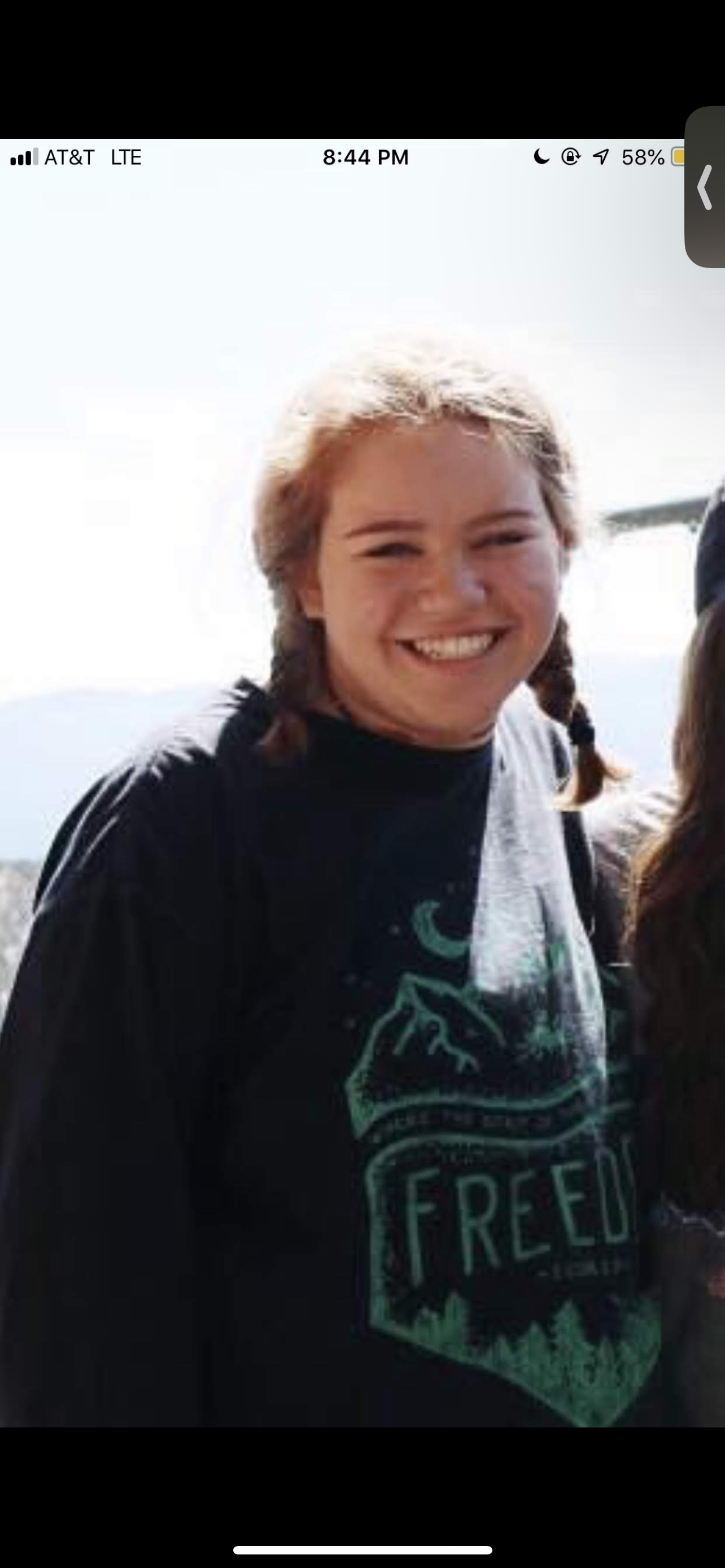 Smiling woman with braided hair wearing a black T-shirt with a mountain and forest graphic