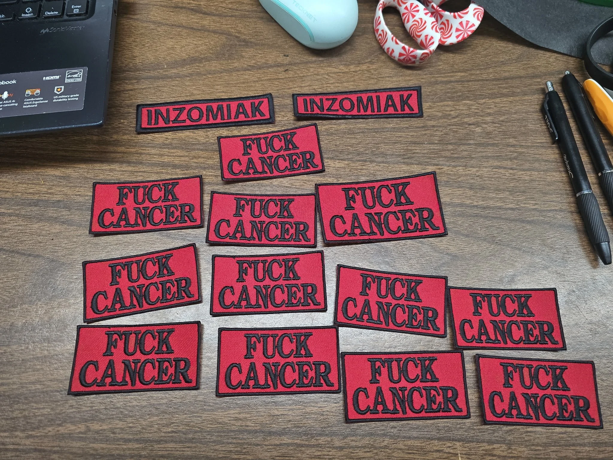 Collection of embroidered patches on a wooden desk with repeated messages of "FUCK CANCER" and two patches with "INZOMIAK".