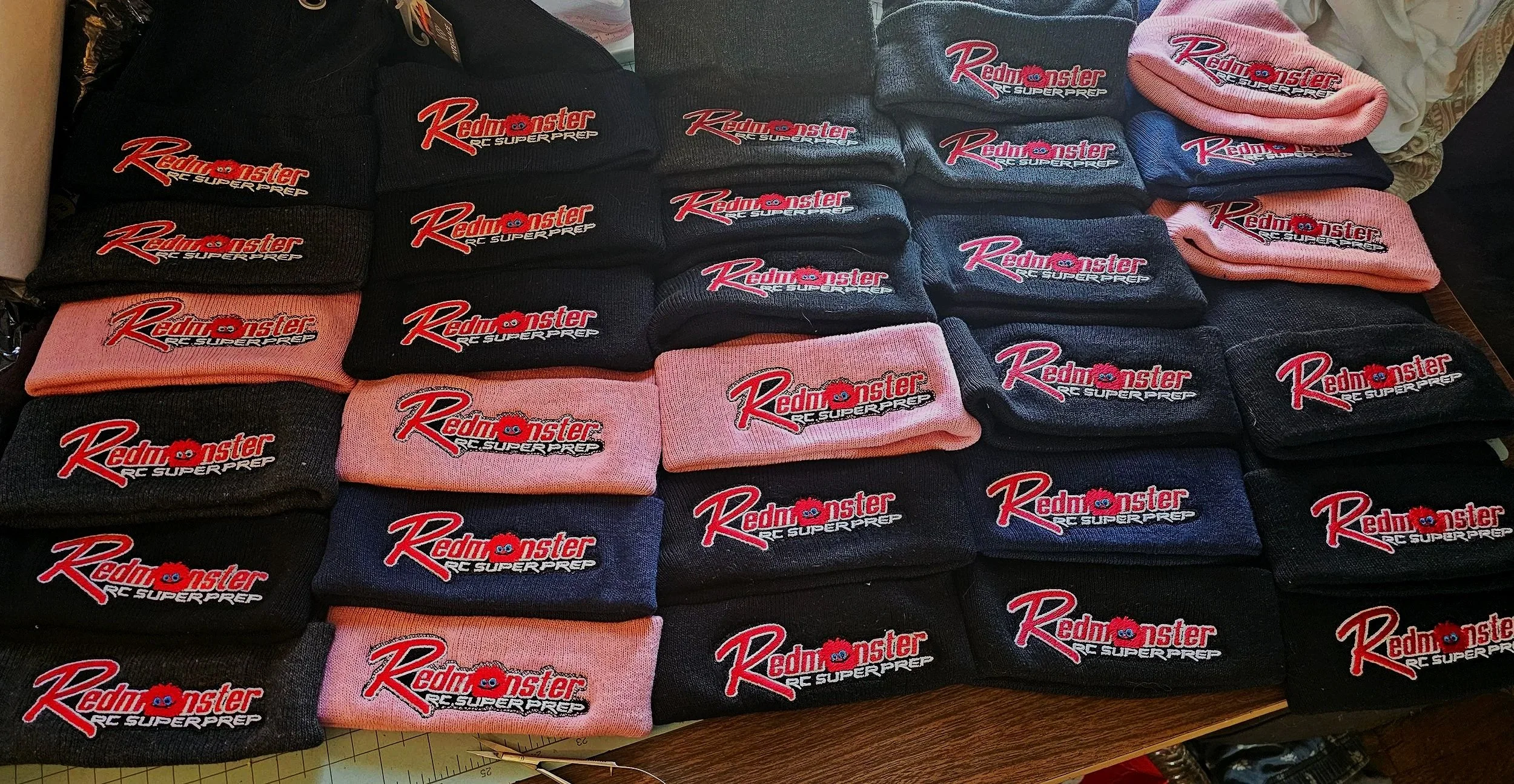 Multiple folded beanies with the logo 'Redmonster RC Superprep' in red and pink, arranged in rows on a table.