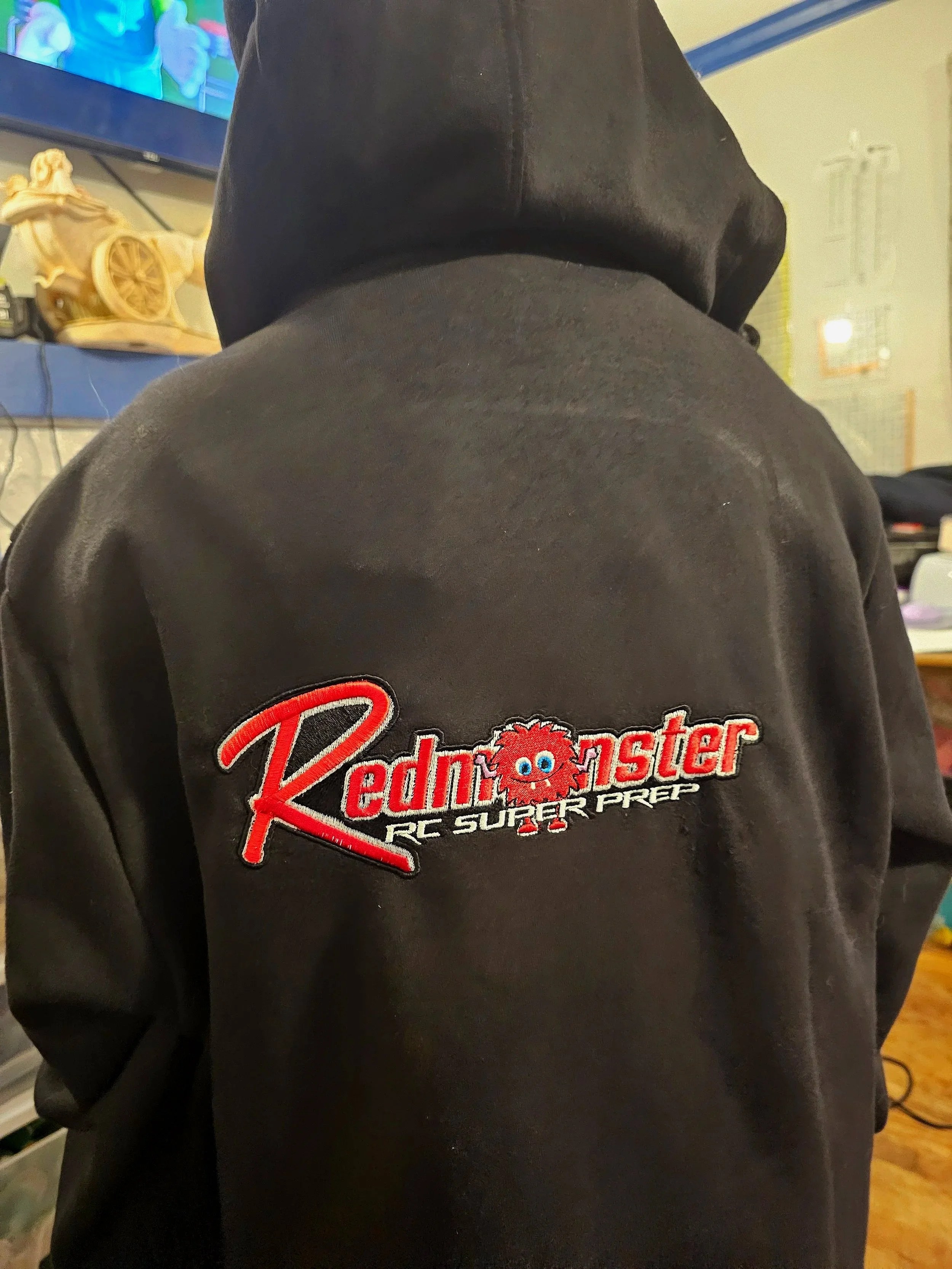 Back of a person wearing a black hoodie with embroidered logo reading 'Rednaster RC Super Prep' with a cartoon red fluffy creature with blue eyes in the middle of the text.