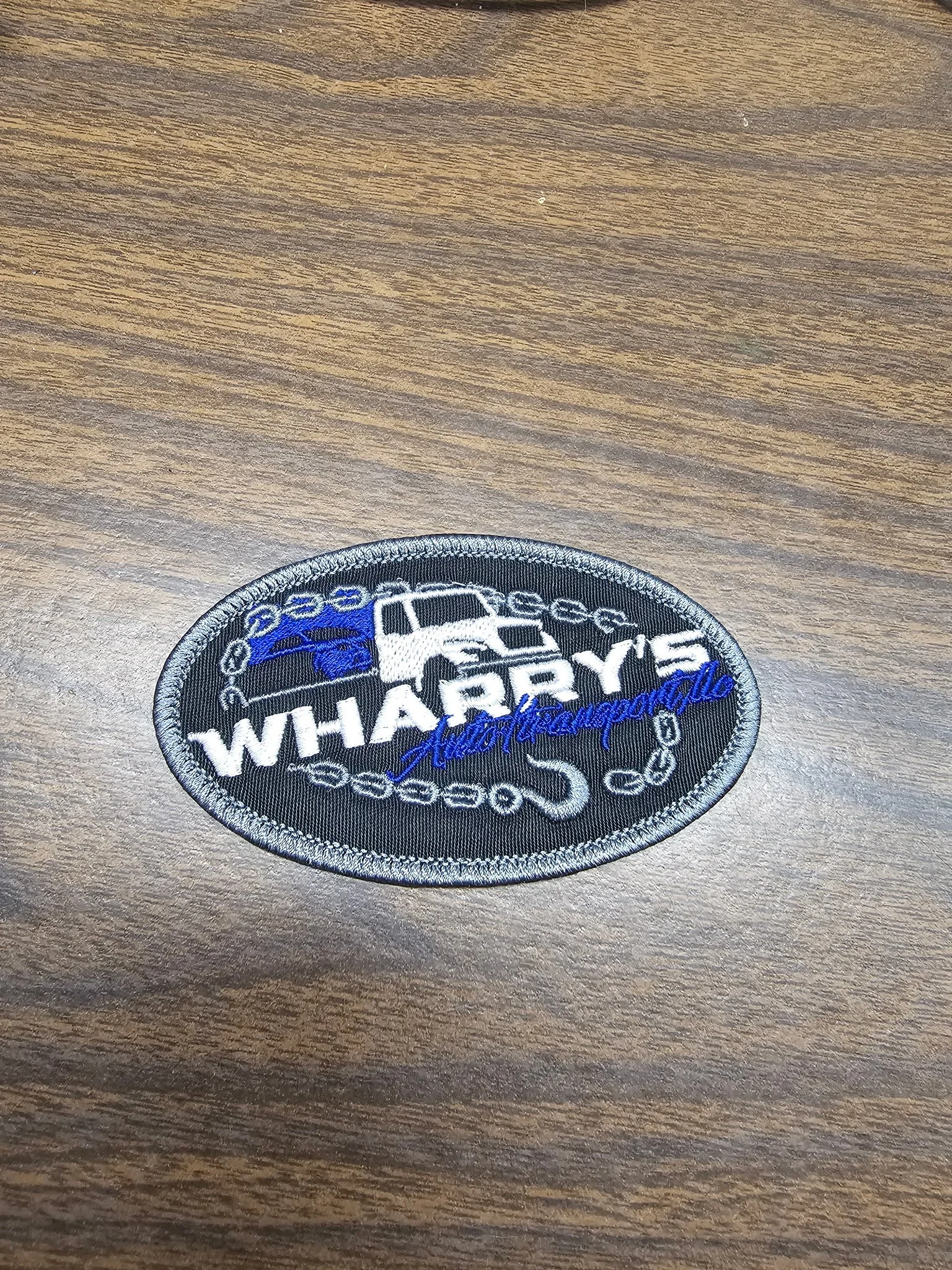 An embroidered patch with the text "Whaterry's" and a signature "K. Cheesecake" on a wooden surface.
