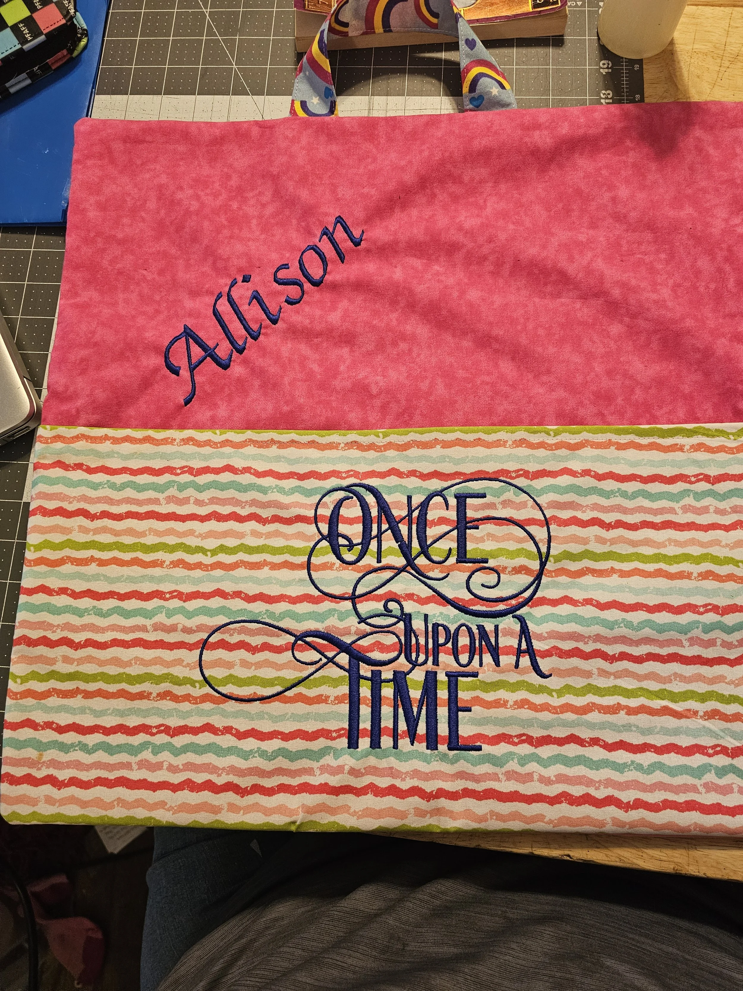 A pink and patterned fabric tote bag with the name Allison embroidered on the pink section and the phrase 'Once Upon a Time' embroidered on the patterned section.