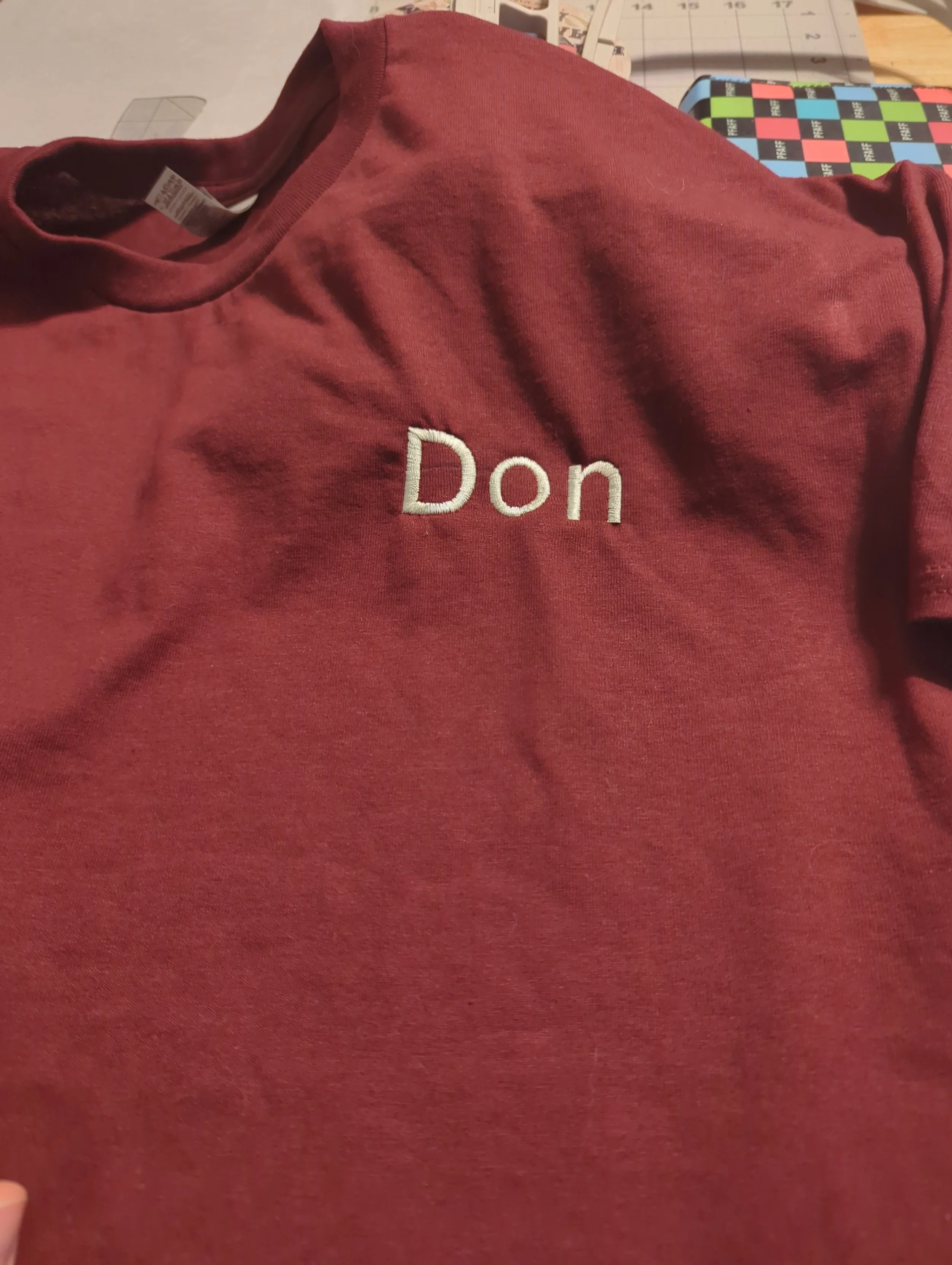 Red T-shirt with the name 'Don' embroidered on it, laid out on a table.