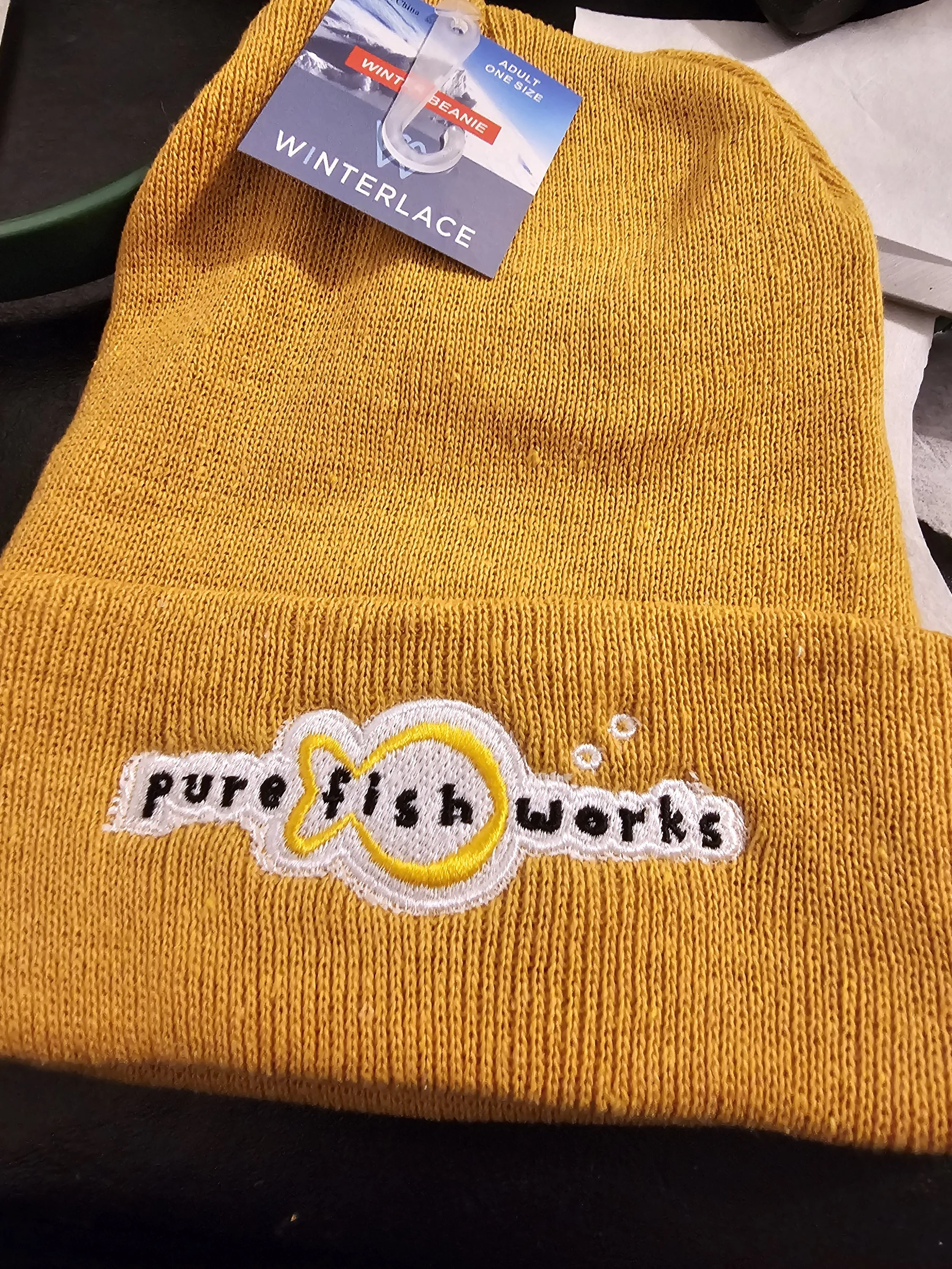 Yellow knit winter beanie hat with a patch that says 'purrs & work' with a fish shape around the word 'fish' and bubbles.