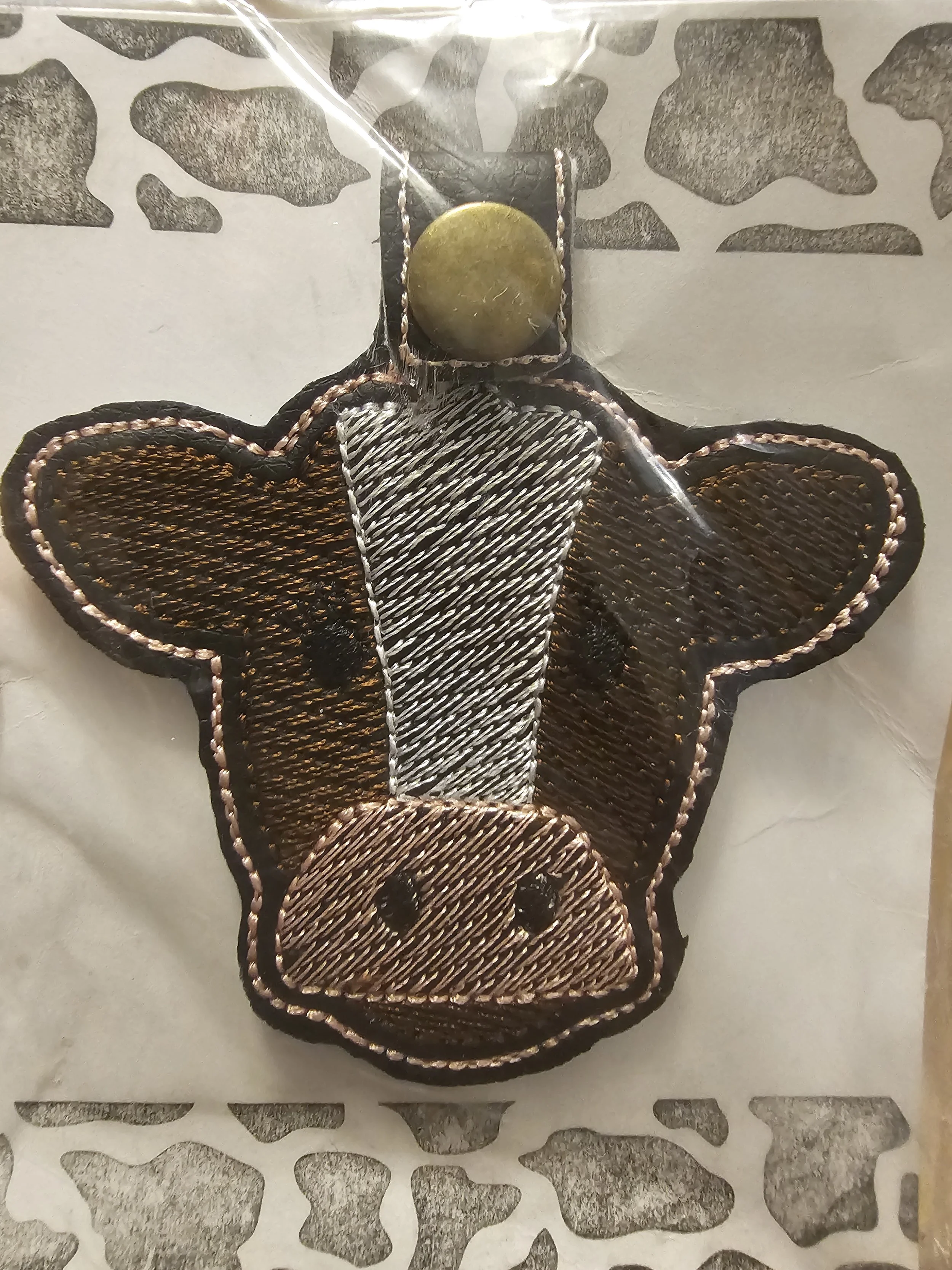 Embroidered patch of a cow's face with a white stripe down the nose and a yellow circle above the head.