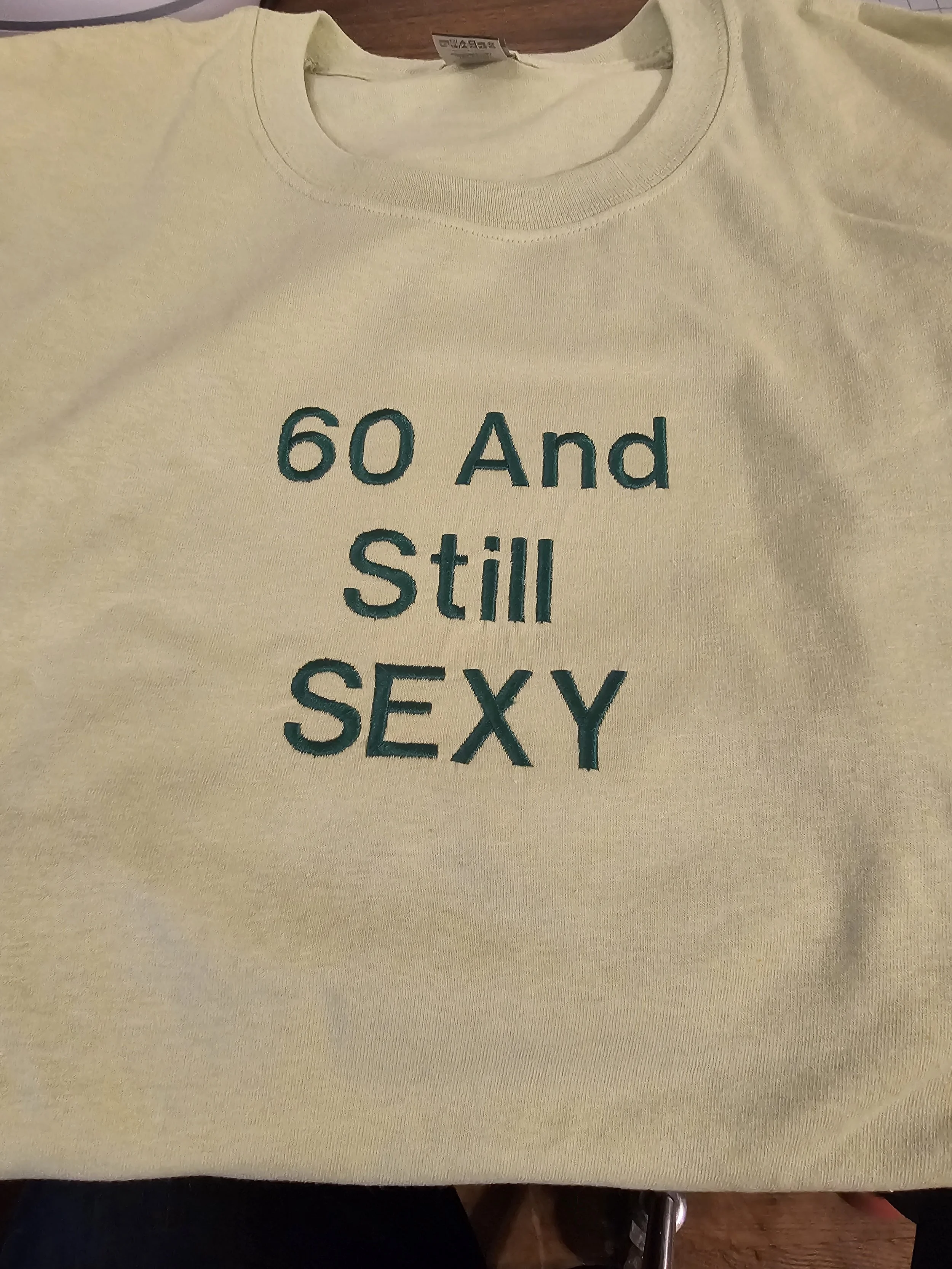 Cream-colored sweatshirt with green text that reads "60 And Still SEXY".
