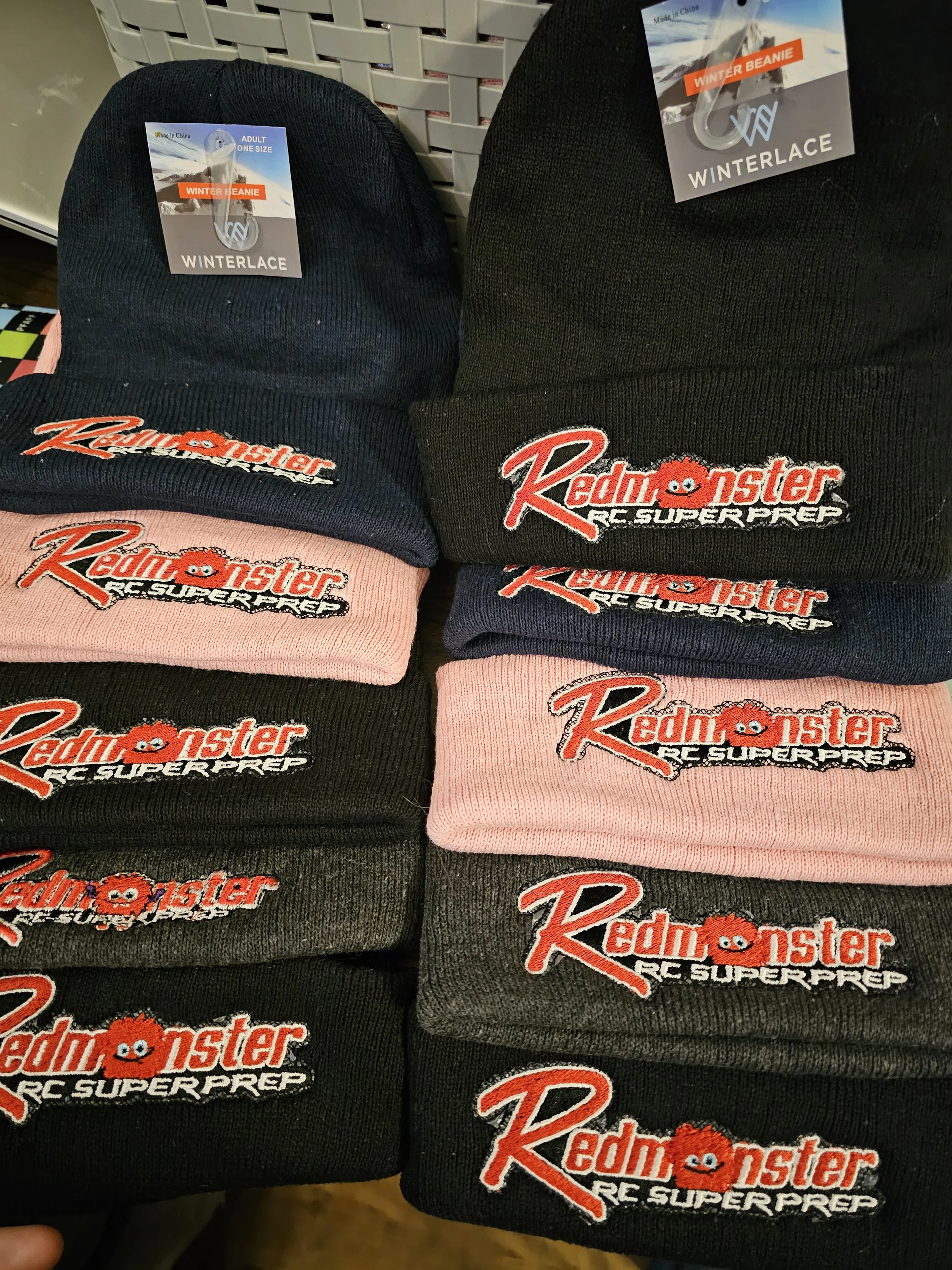 Stacked winter beanies with Redmonster RC Superprep logos, in black, pink, and dark gray colors, on display at a store.