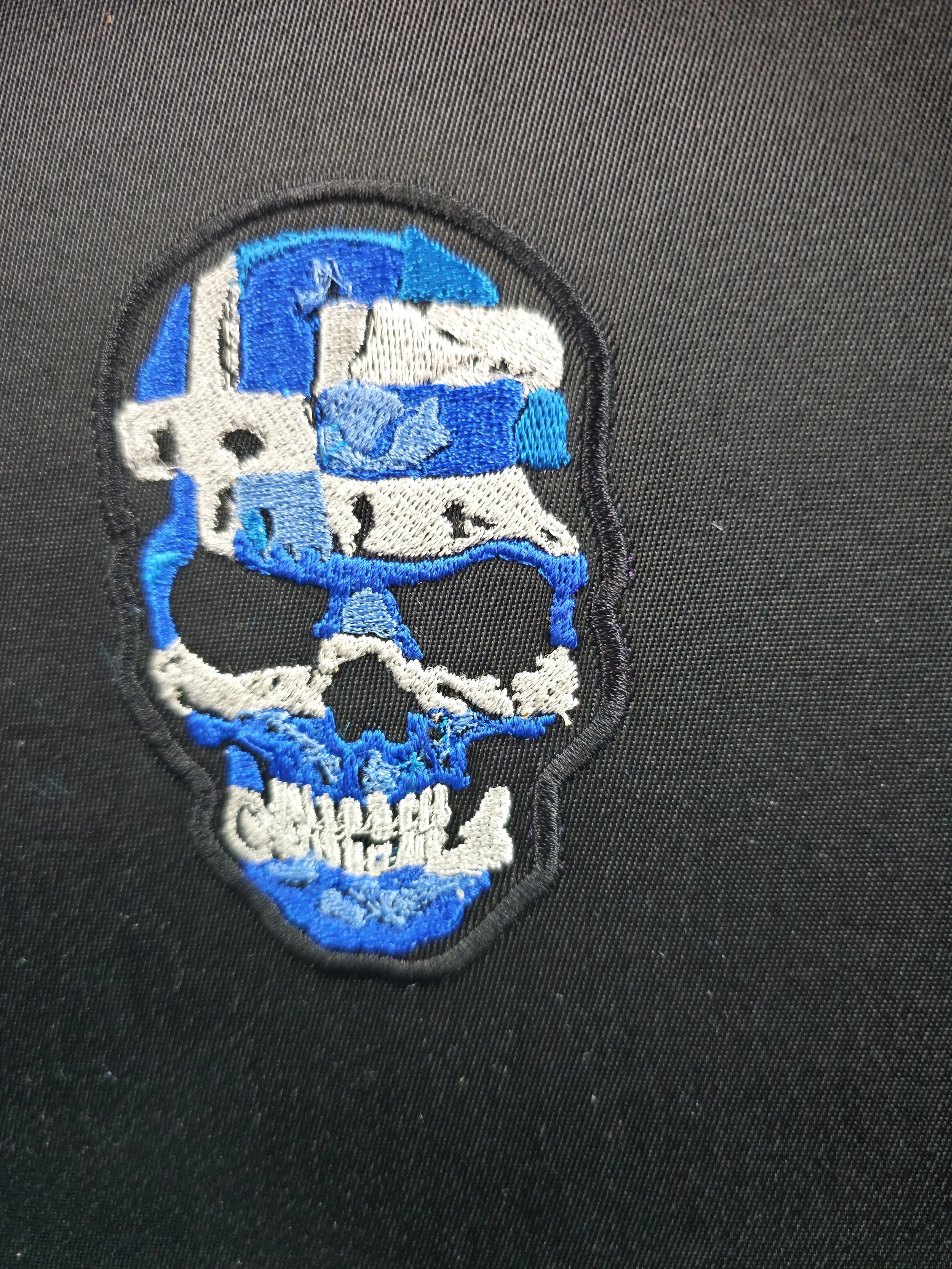 Embroidered patch of a skull with blue and white details on black fabric.