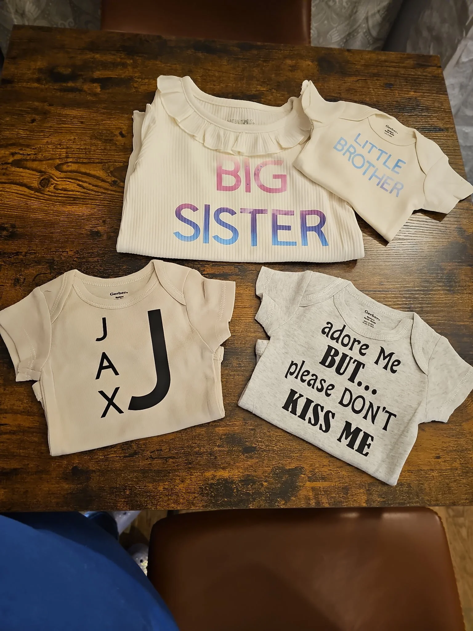 Four baby onesies with printed texts on a wooden table.