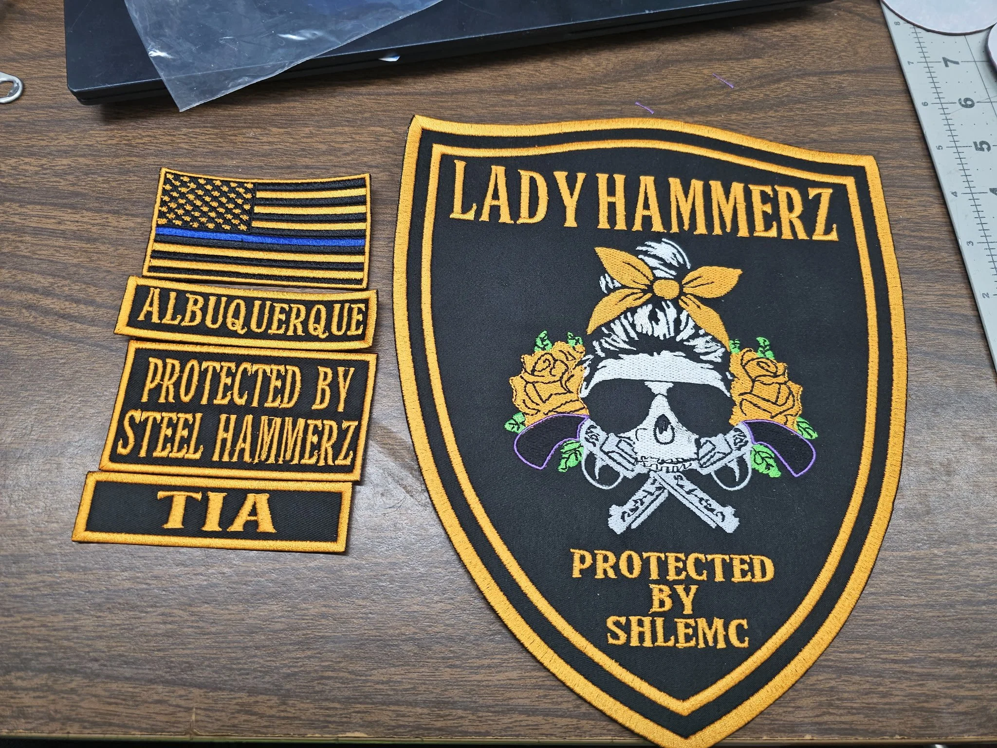 Embroidered patches with an American flag featuring a blue line, a patch reading "ALBUQUERQUE PROTECTED BY STEEL HAMMERZ," and a large shield-shaped patch with skull, flowers, and the text "LADY HAMMERZ PROTECTED BY SALEMC".