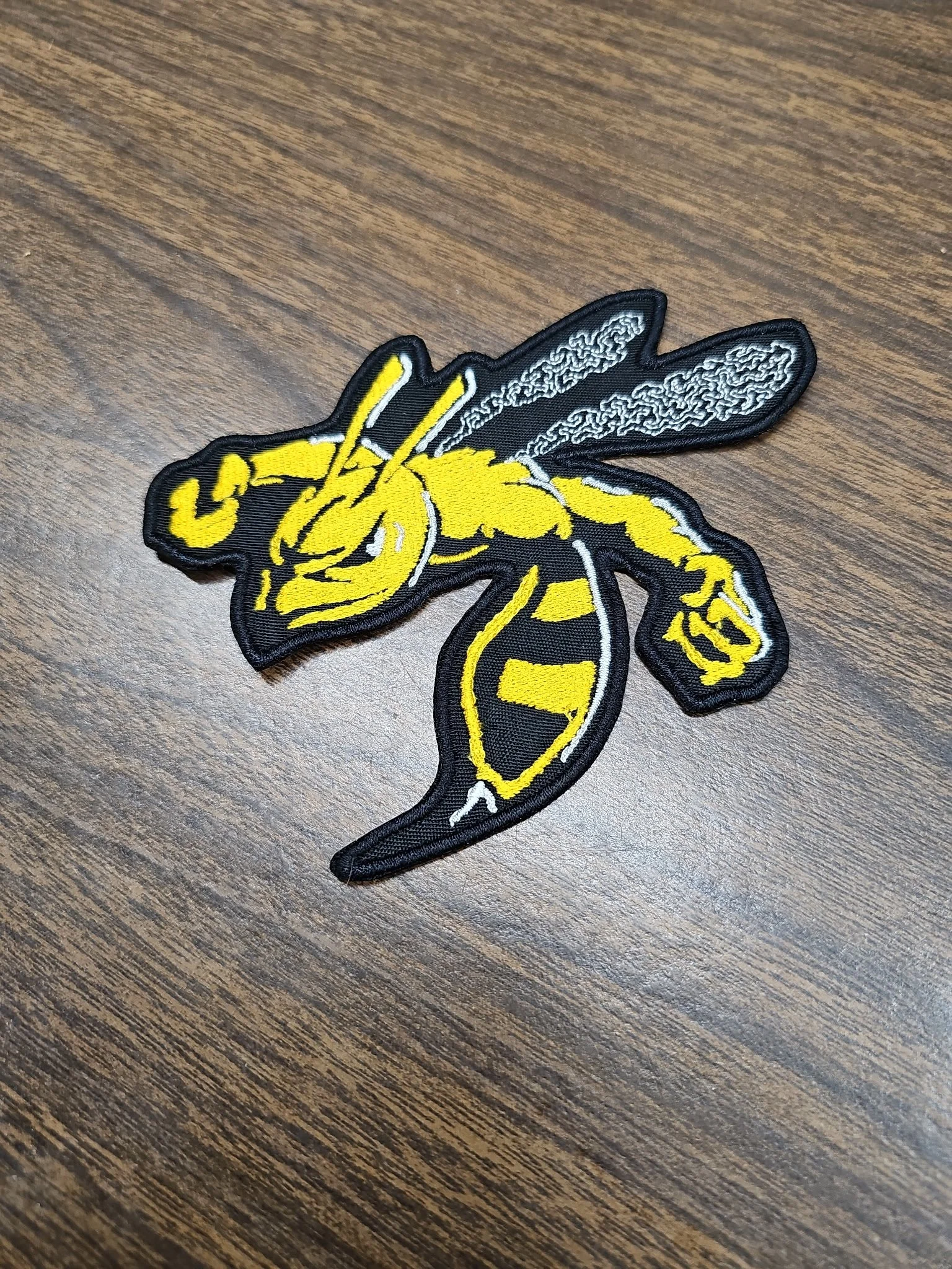 embroidered patch of a yellow and black hornet on a dark wood surface