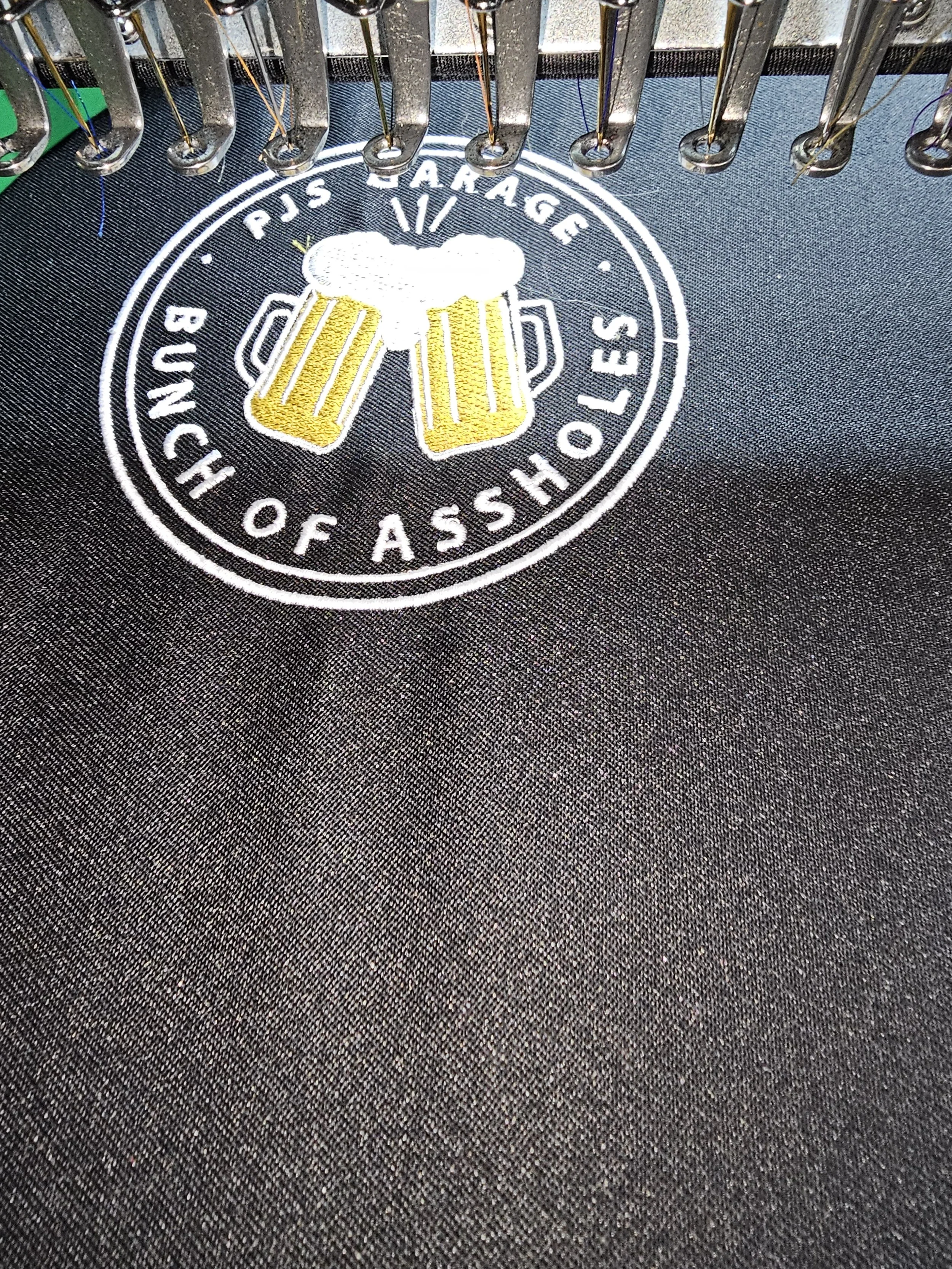 Embroidery of a beer mug with foam over a circular logo that reads 'PJS Garage' and 'Bunch of Assholes'.