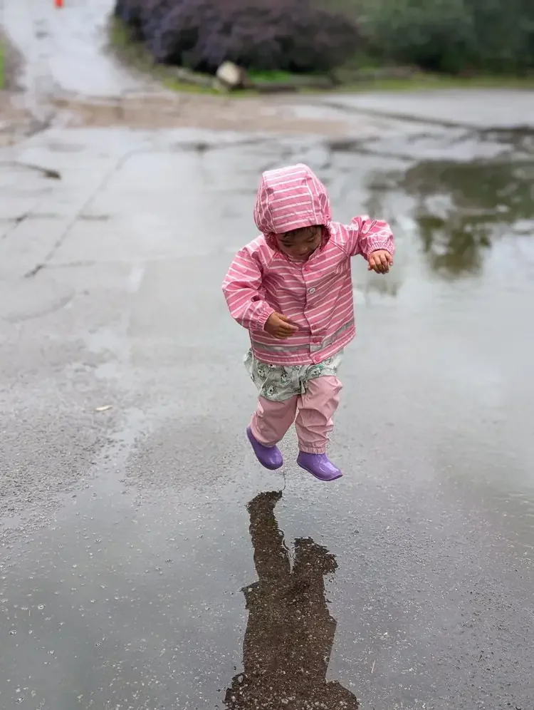 Child jumping in a rain puddle during outdoor learning at Greenwood Trail Forest School in San Francisco.
