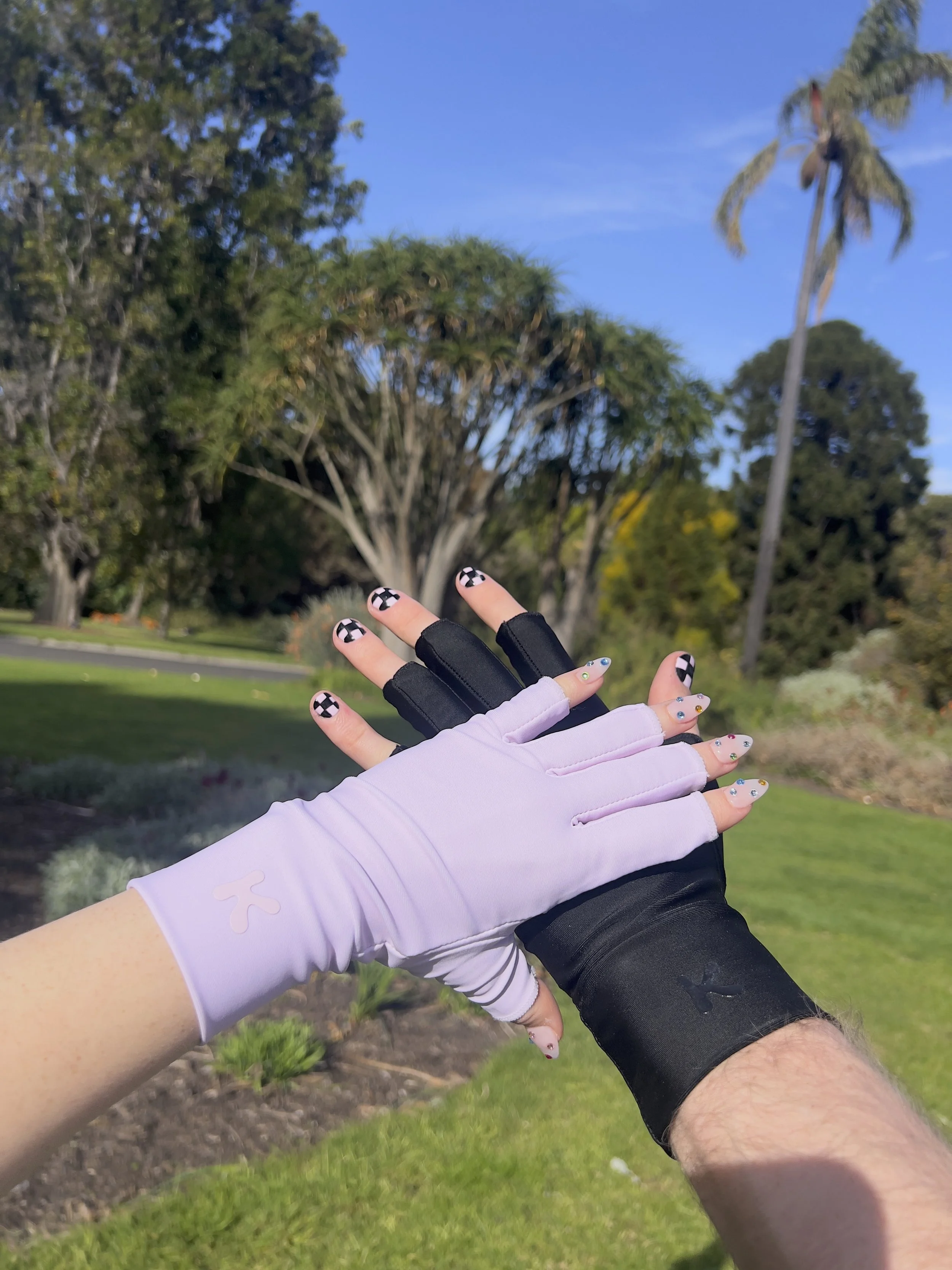Two people wearing gloves, one in a white glove and the other in a black glove, giving a high-five outdoors in a park with trees and a blue sky in the background.