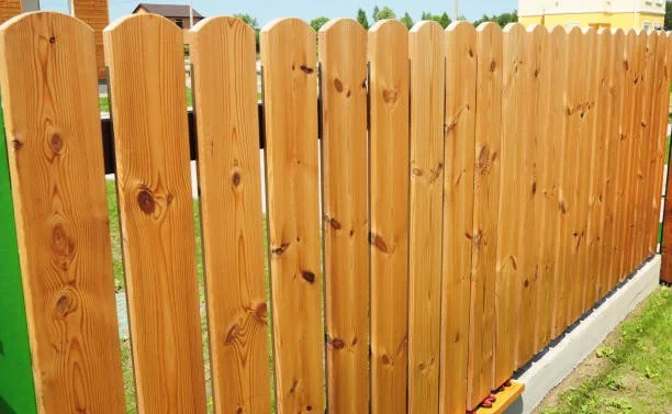 Wooden picket fence in a backyard with grass and a concrete base.