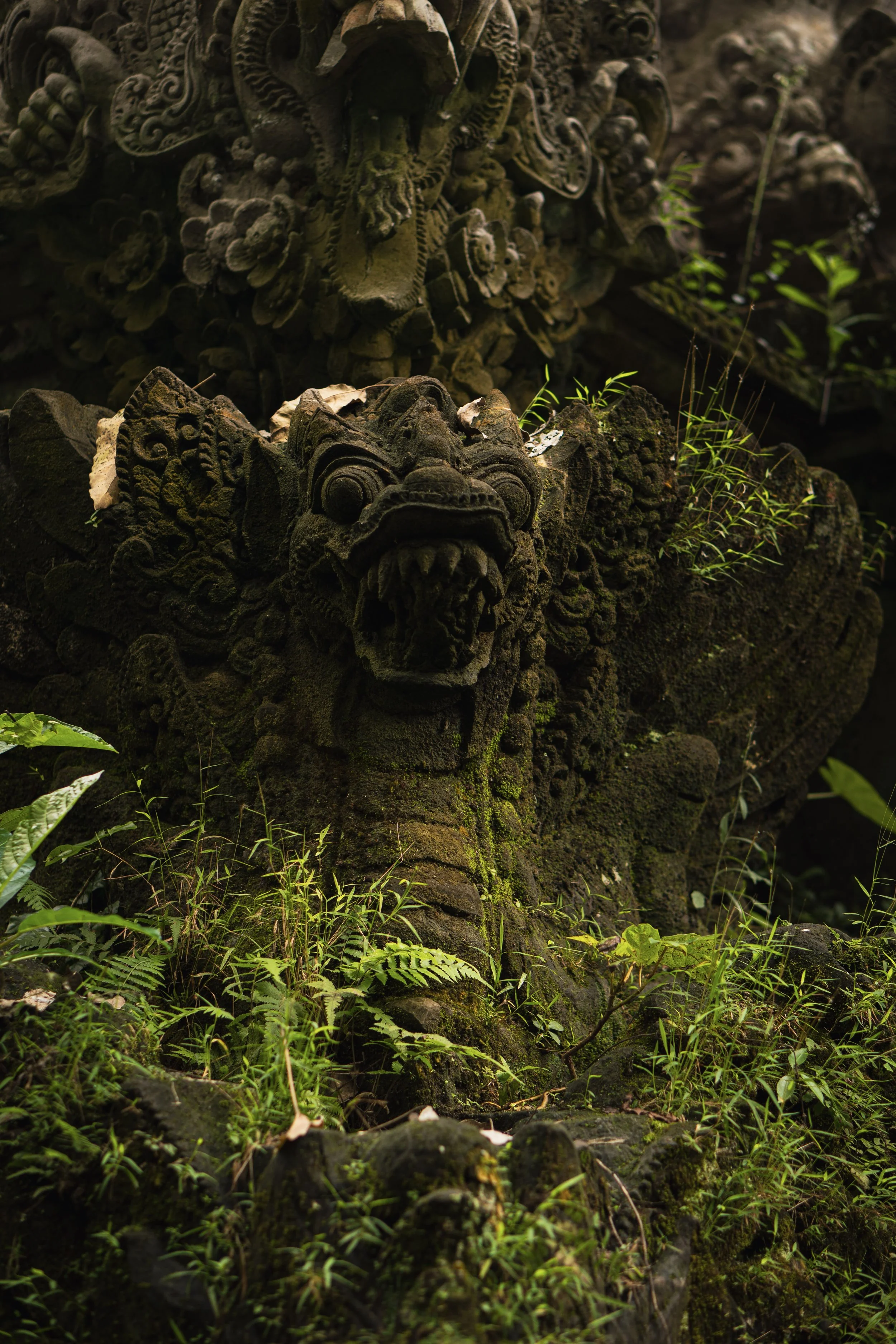 Statues traditionnelles en pierre couvrant de mousse et d'herbes vertes, représentant des figures avec des yeux et des bouches sculptés, dans un environnement naturel.