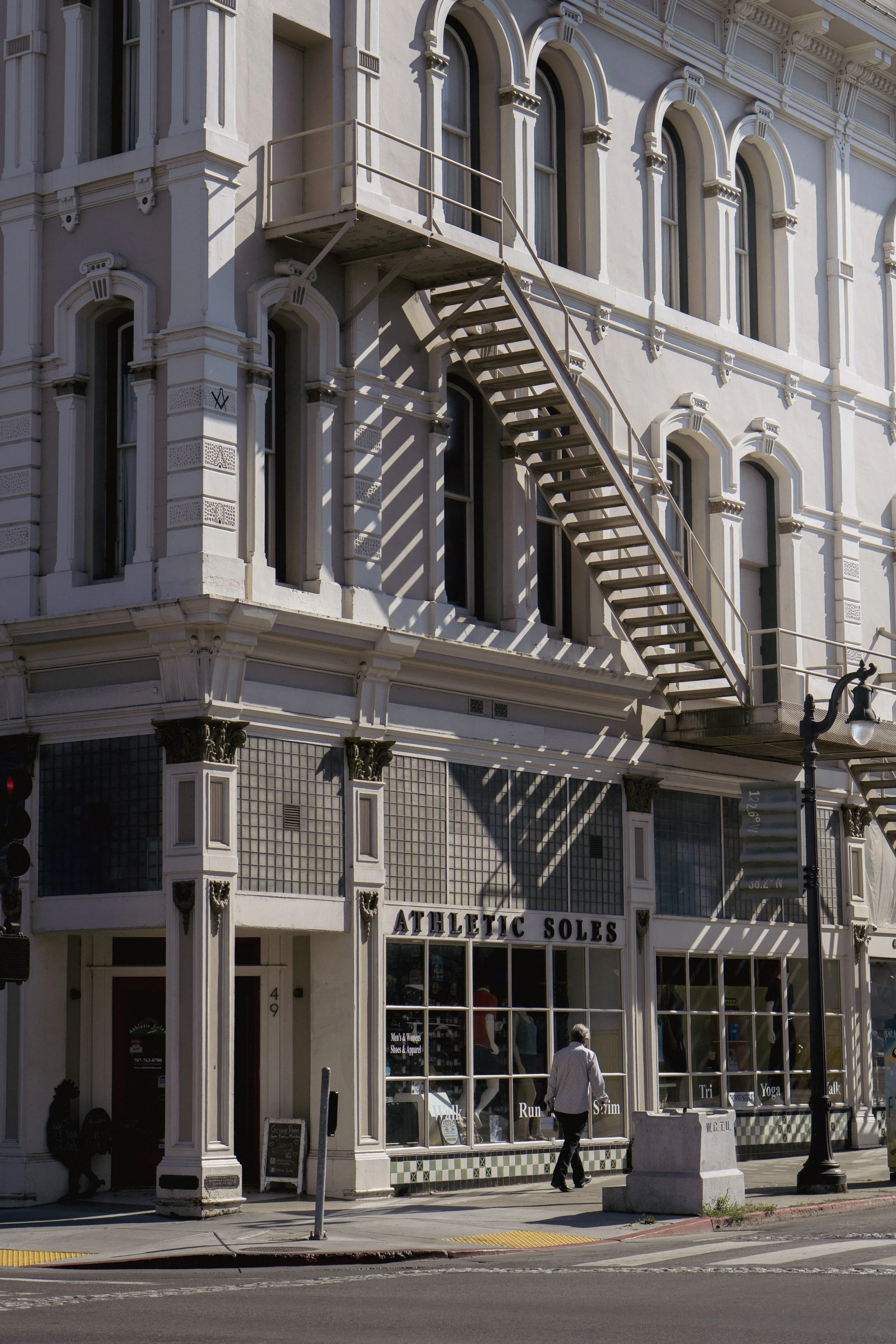 Bâtiment historique avec façade blanche, escaliers de secours en métal, magasin Athletique Soles, personnes marchant devant.