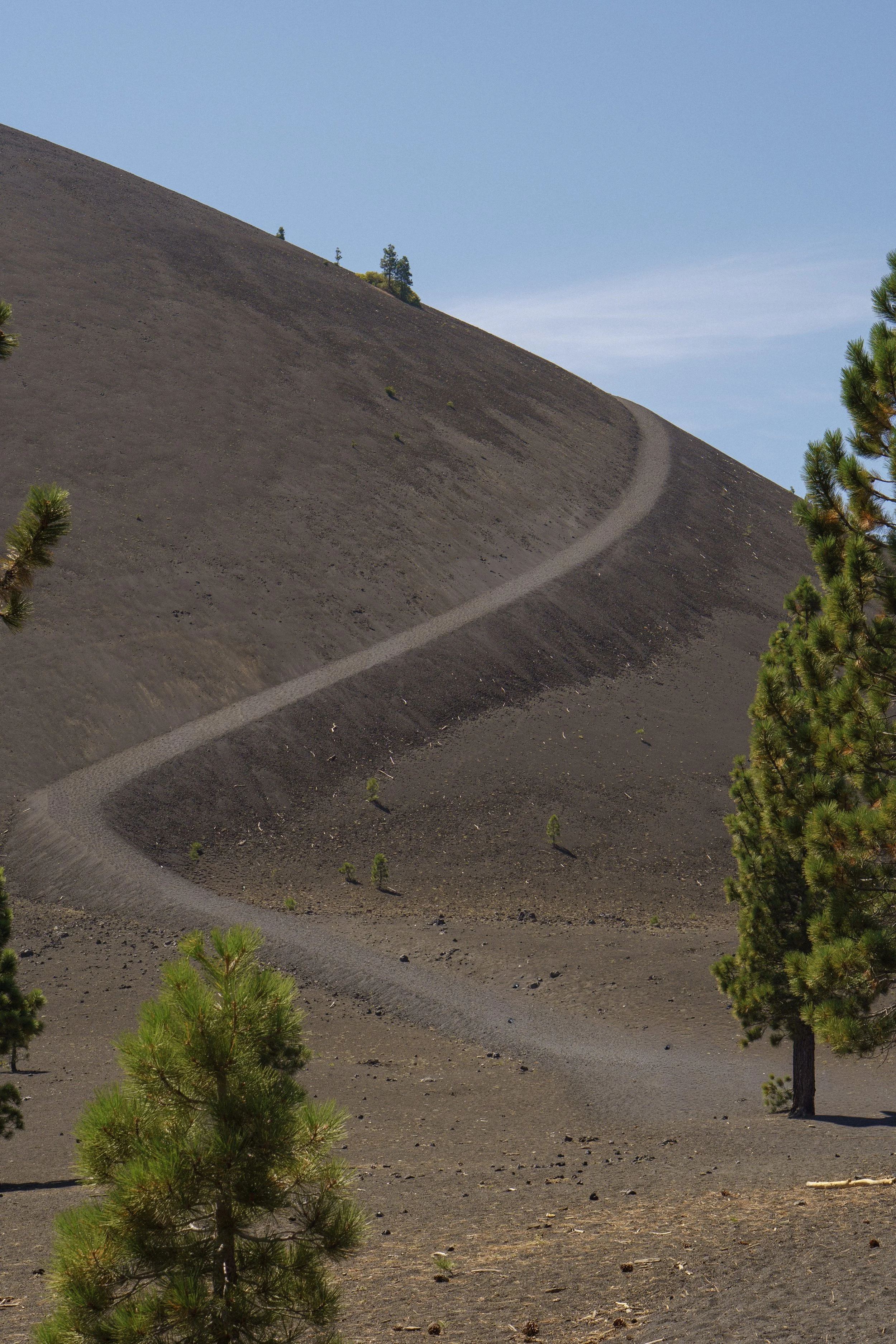 Une montagne aride avec un sentier serpentant en zigzag, entourée de quelques arbres verts.