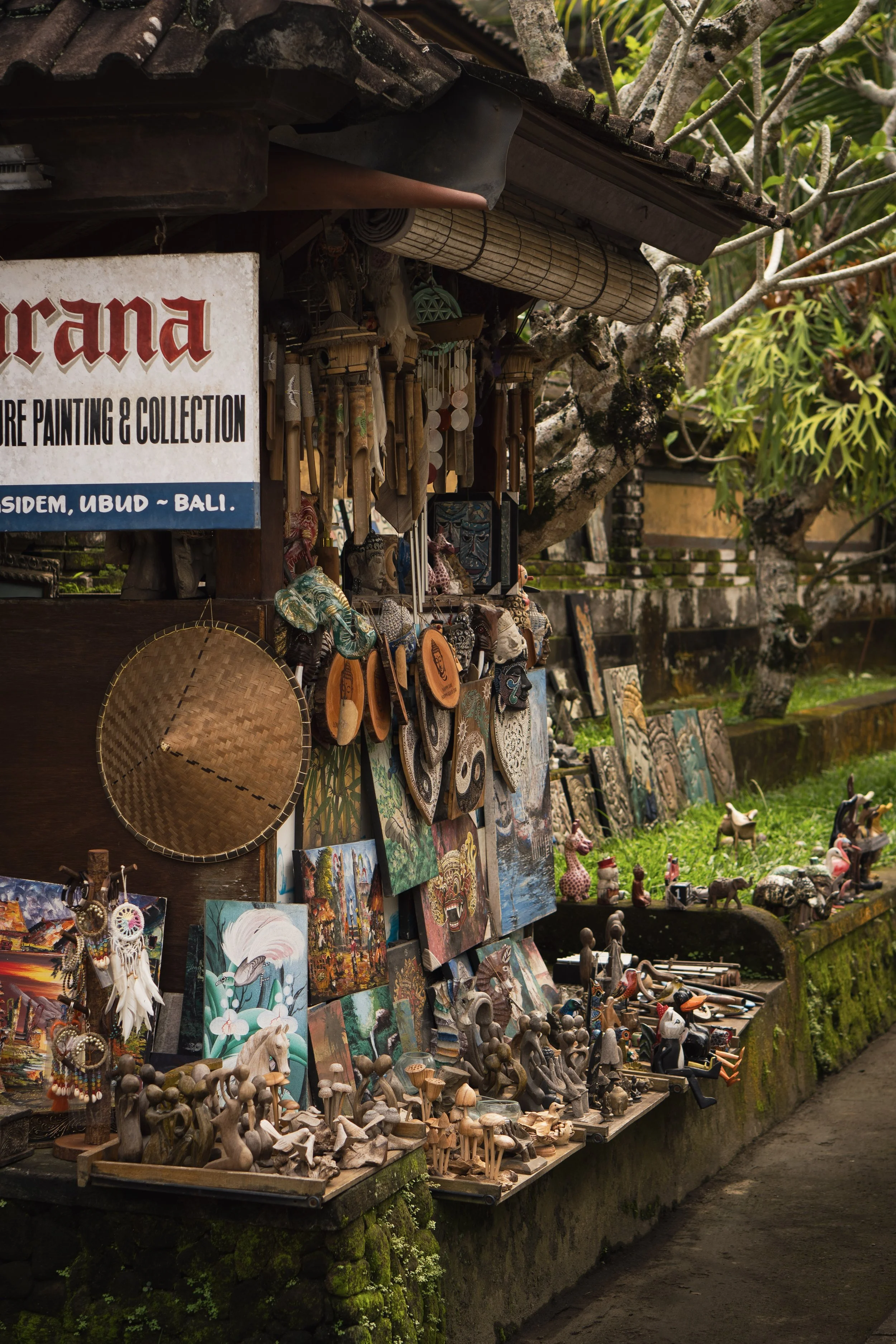 Vente de souvenirs et d'œuvres d'art traditionnelles balinaises, avec peintures, sculptures en bois, bijoux et objets artisanaux dans un stand en plein air à Ubud, Bali, entouré de végétation luxuriante.