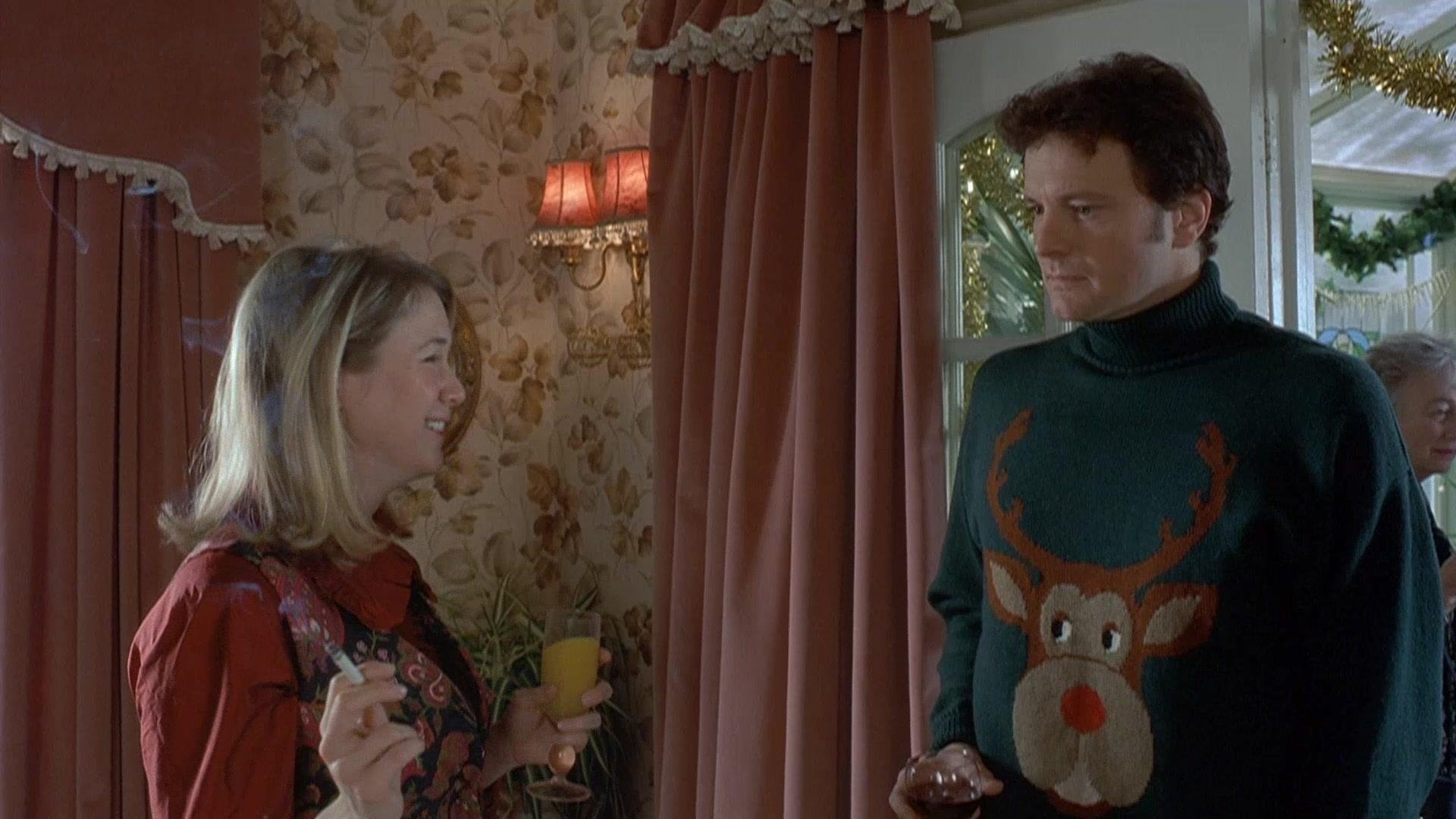 Bridget  Jonse holding a glass and  a cigarette, smiling and talking to Mark Darcy wearing a Christmas sweater with a reindeer's face on it, indoors with floral wallpaper, pink curtains, and a window with a view of a backyard.