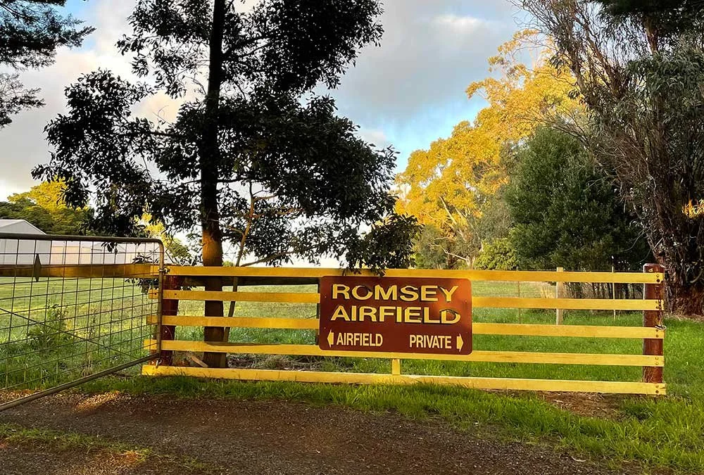 Gate with a sign that reads 'Romsey Airfield - Airfield Private' blocking entry, with trees and grass in the background.