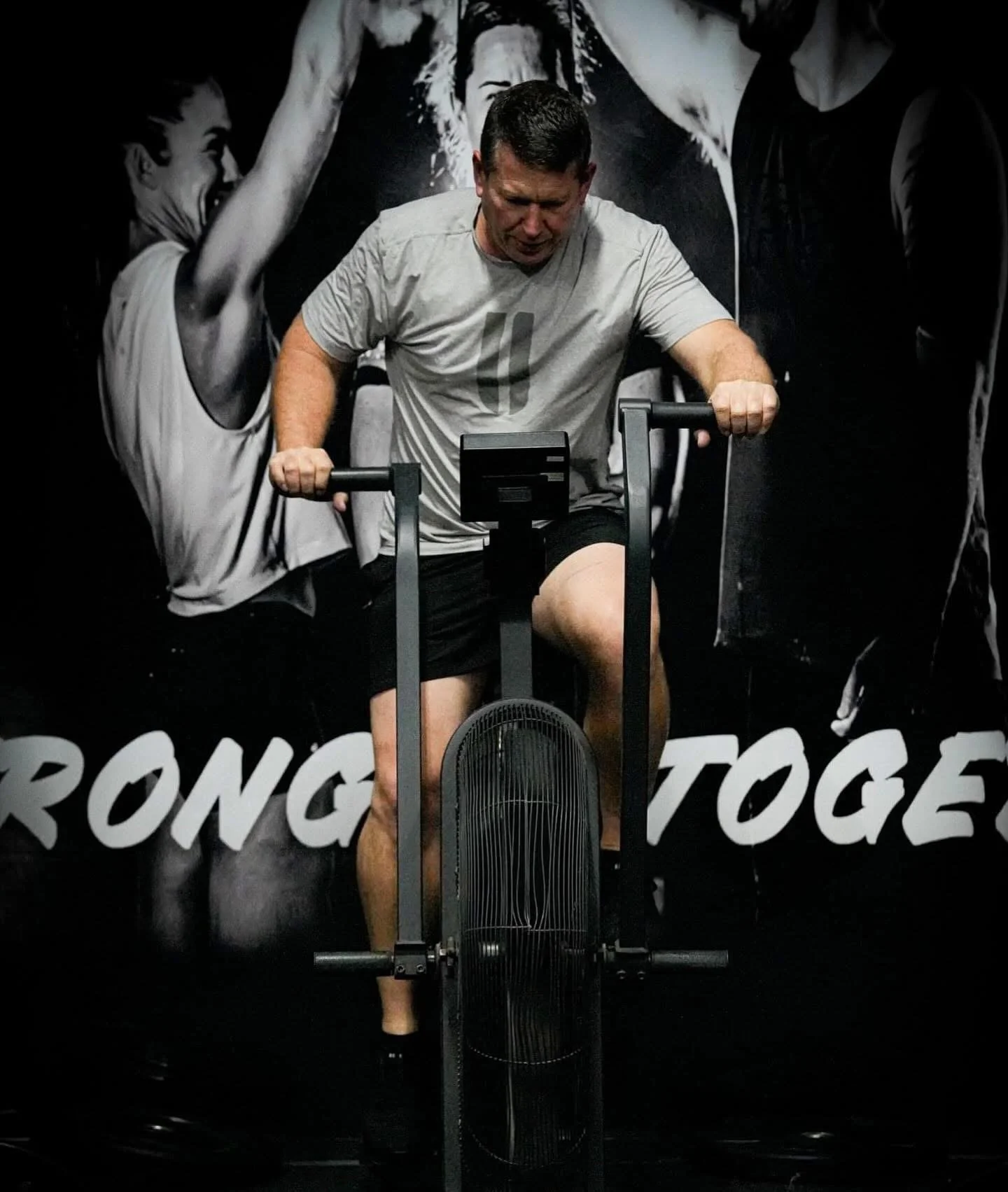 Man riding a stationary exercise bike in a gym with a black and white motivational poster behind him.
