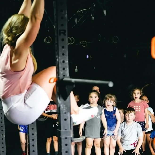 Young girl performing a leg raise on gym rings while a group of children watch