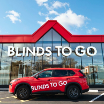 Red vehicle parked in front of a store with a sign that says 'Blinds To Go' on the building's glass facade. The store has a red roof and large windows, under a partly cloudy sky. HVAC Services New York City, USA.