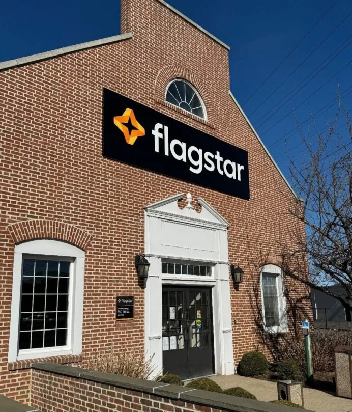 The image shows a brick building with a black sign reading 'flagstar' and a star logo on it, with a clear blue sky in the background. HVAC Services New York City, USA.